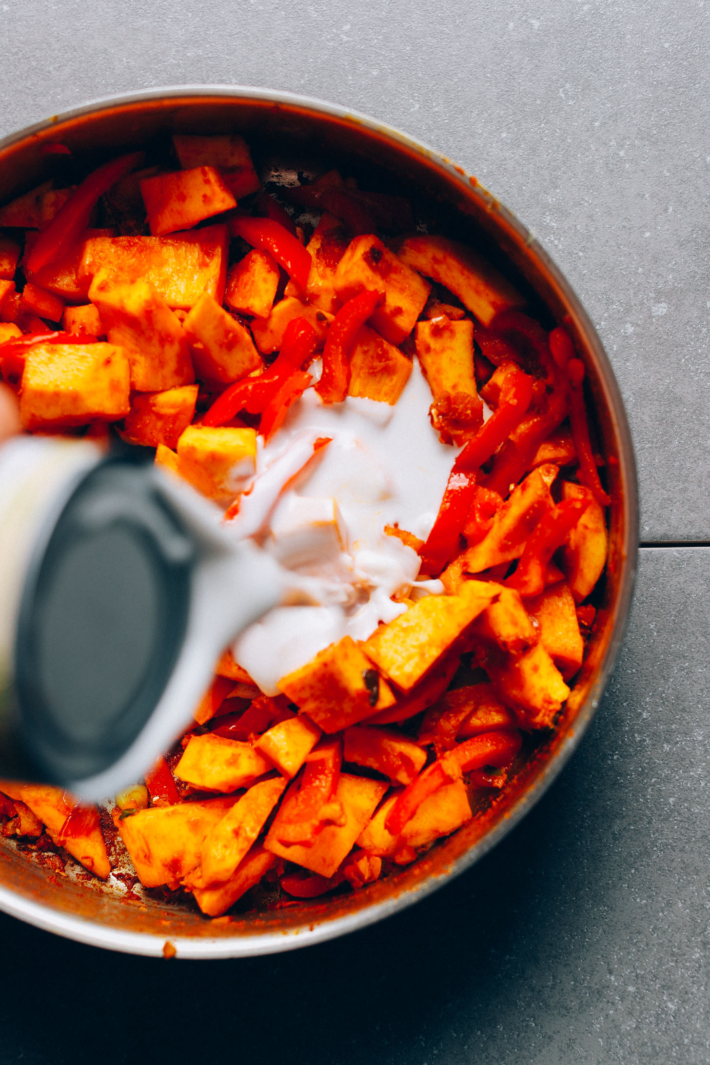 Pouring coconut milk into cooking pan filled with veggies and spices for vegan Yellow Pumpkin Curry