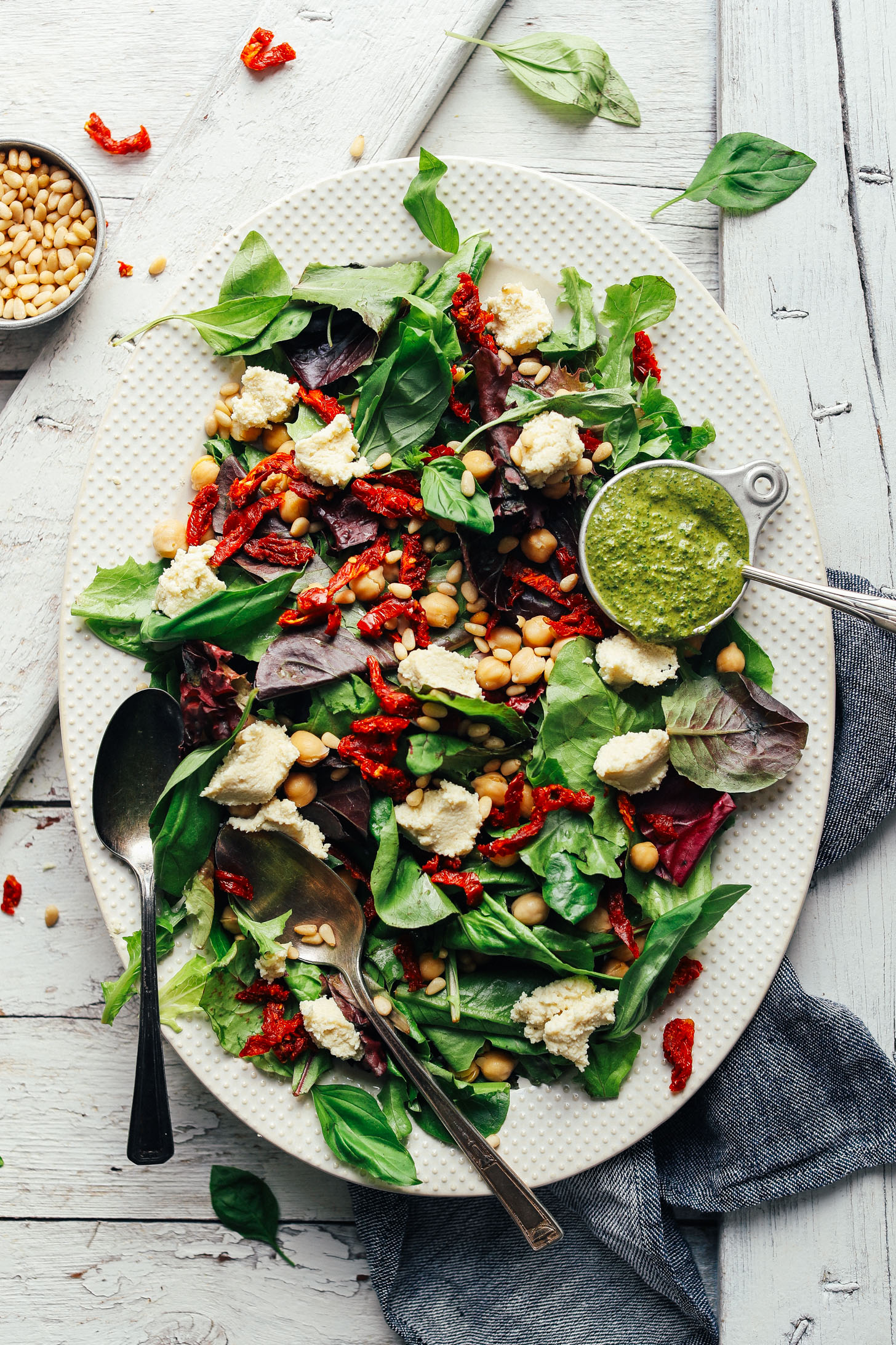Large white serving platter loaded with our recipe for Green Salad with Almond Ricotta, Vibrant Pesto, and Sun-Dried Tomatoes
