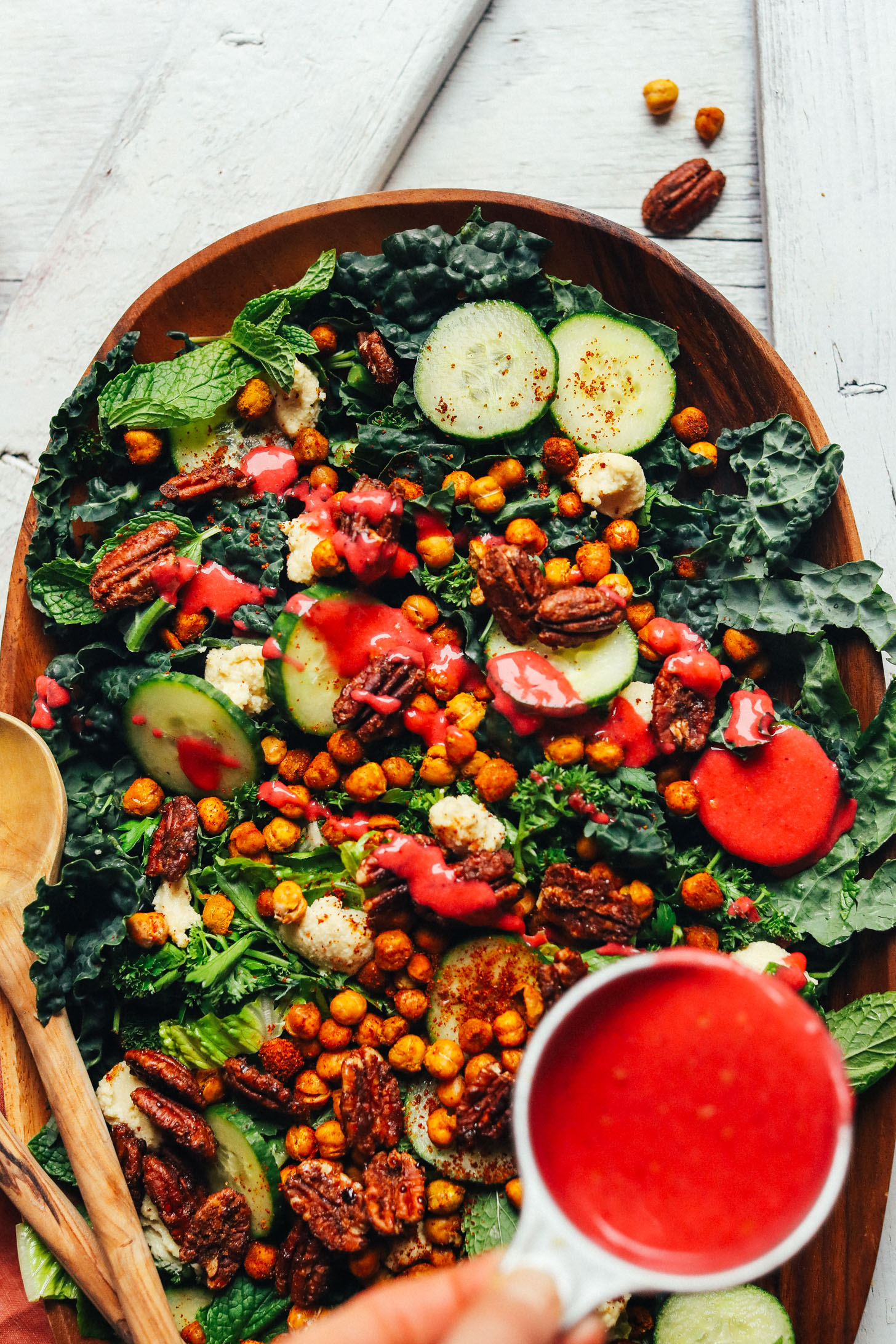 Drizzling Cranberry Vinaigrette over a large wooden platter filled with Herbed Green Salad