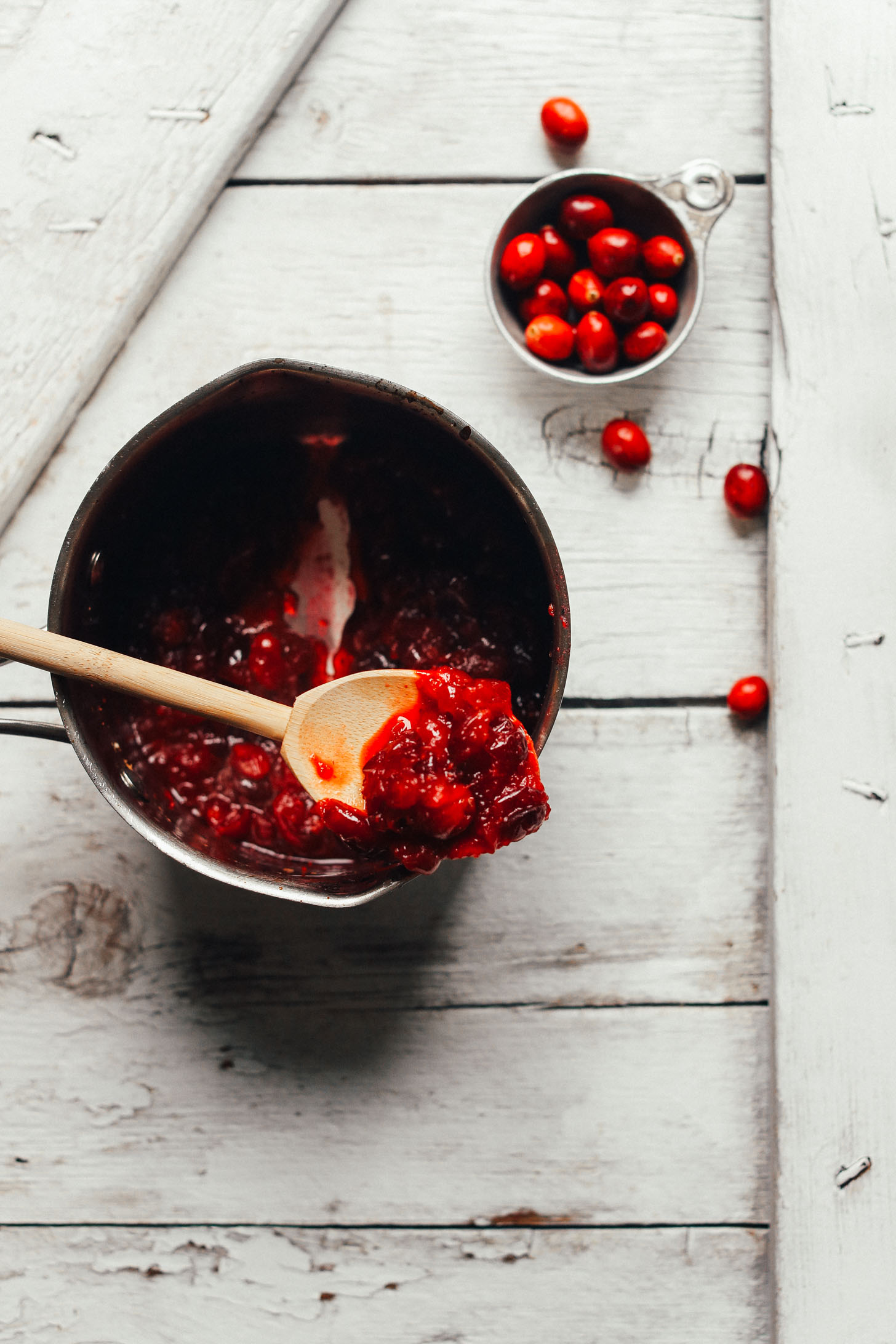 Wooden spoon holding up freshly cooked cranberries from a saucepan