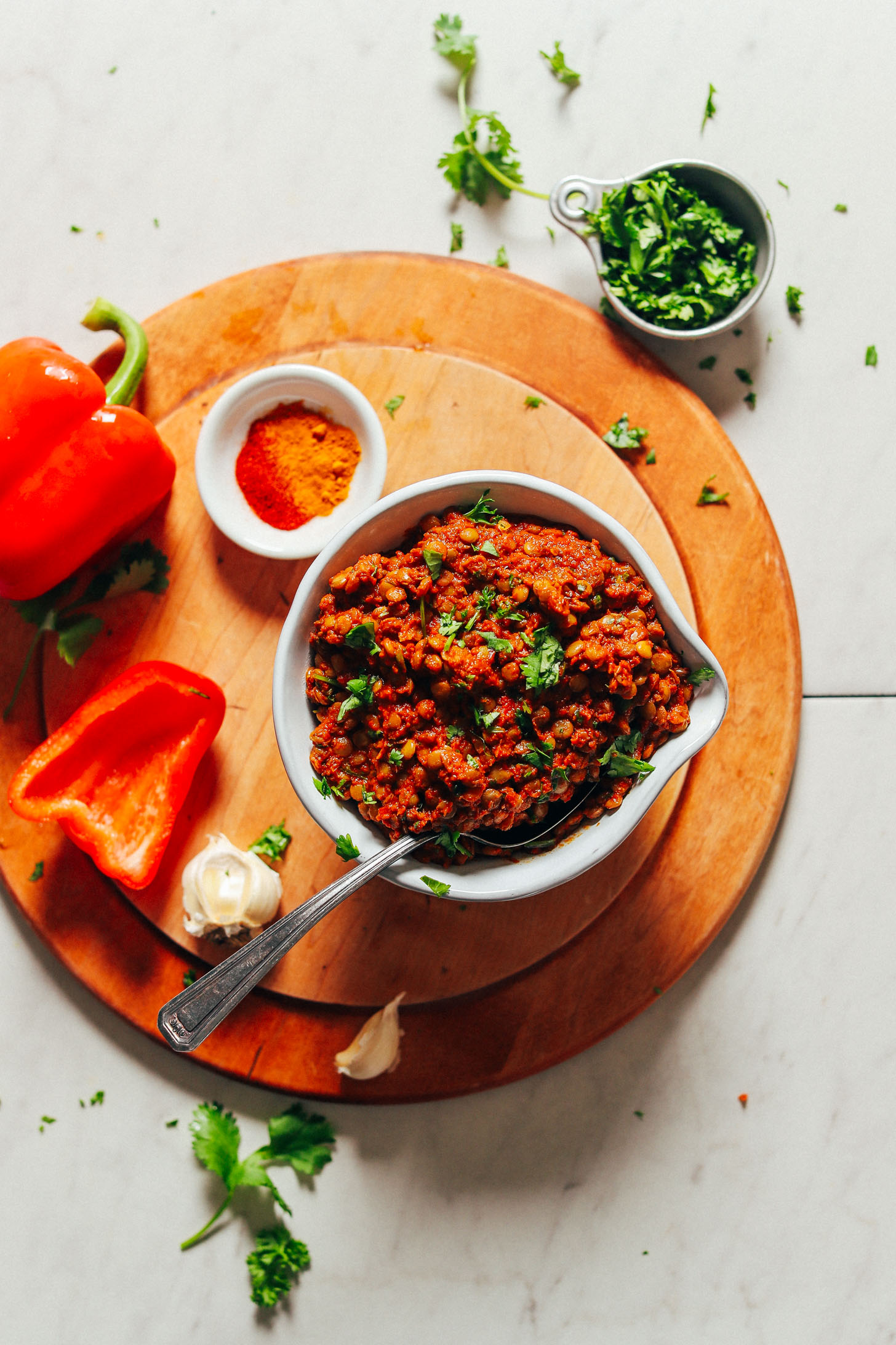 Big bowl of Moroccan Spiced Lentils surrounded by red bell pepper, garlic, fresh parsley, cilantro, and spices