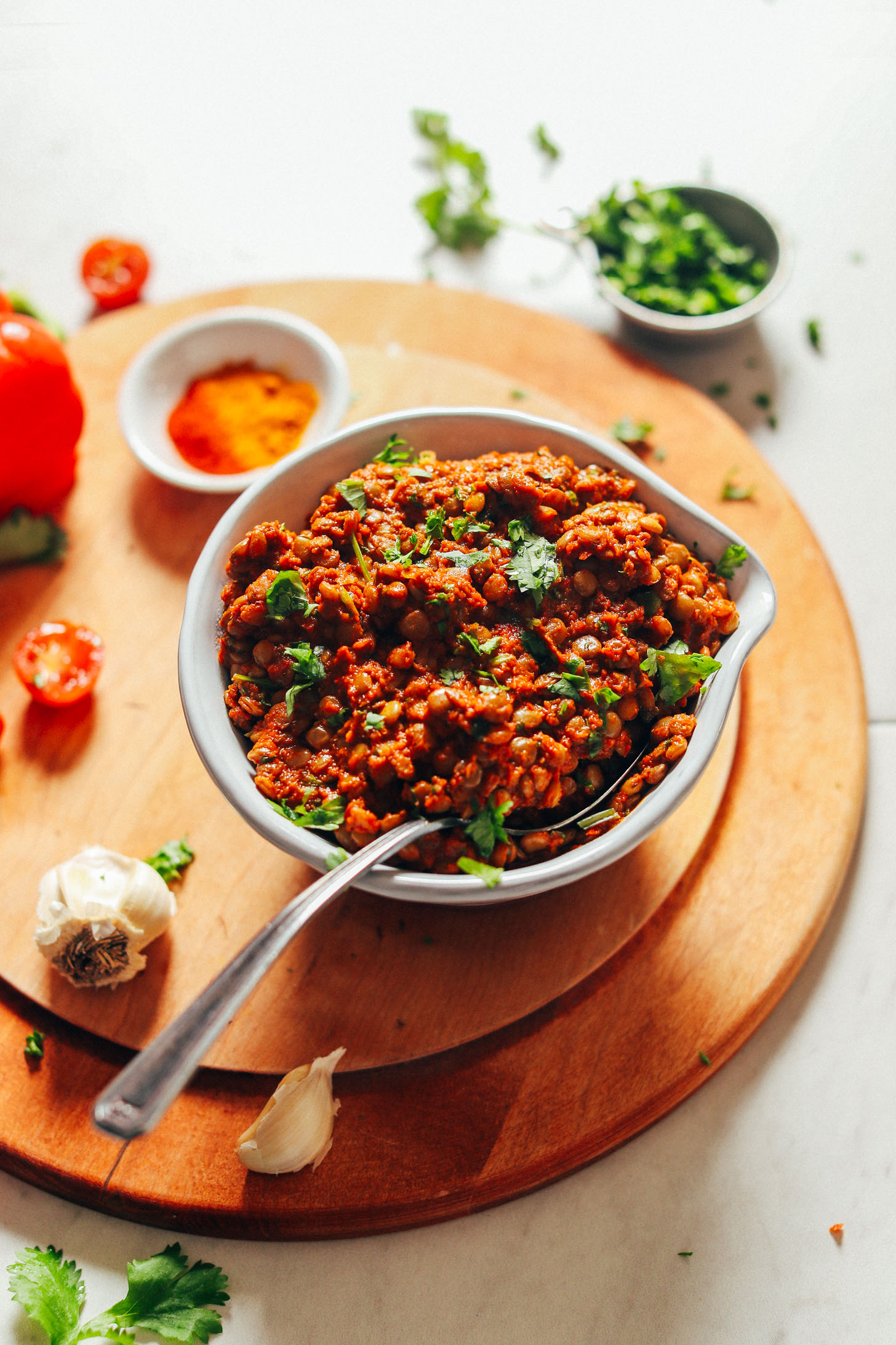 Close up shot of a big bowl of Moroccan-Spiced Lentils on a wood cutting board with fresh ingredients