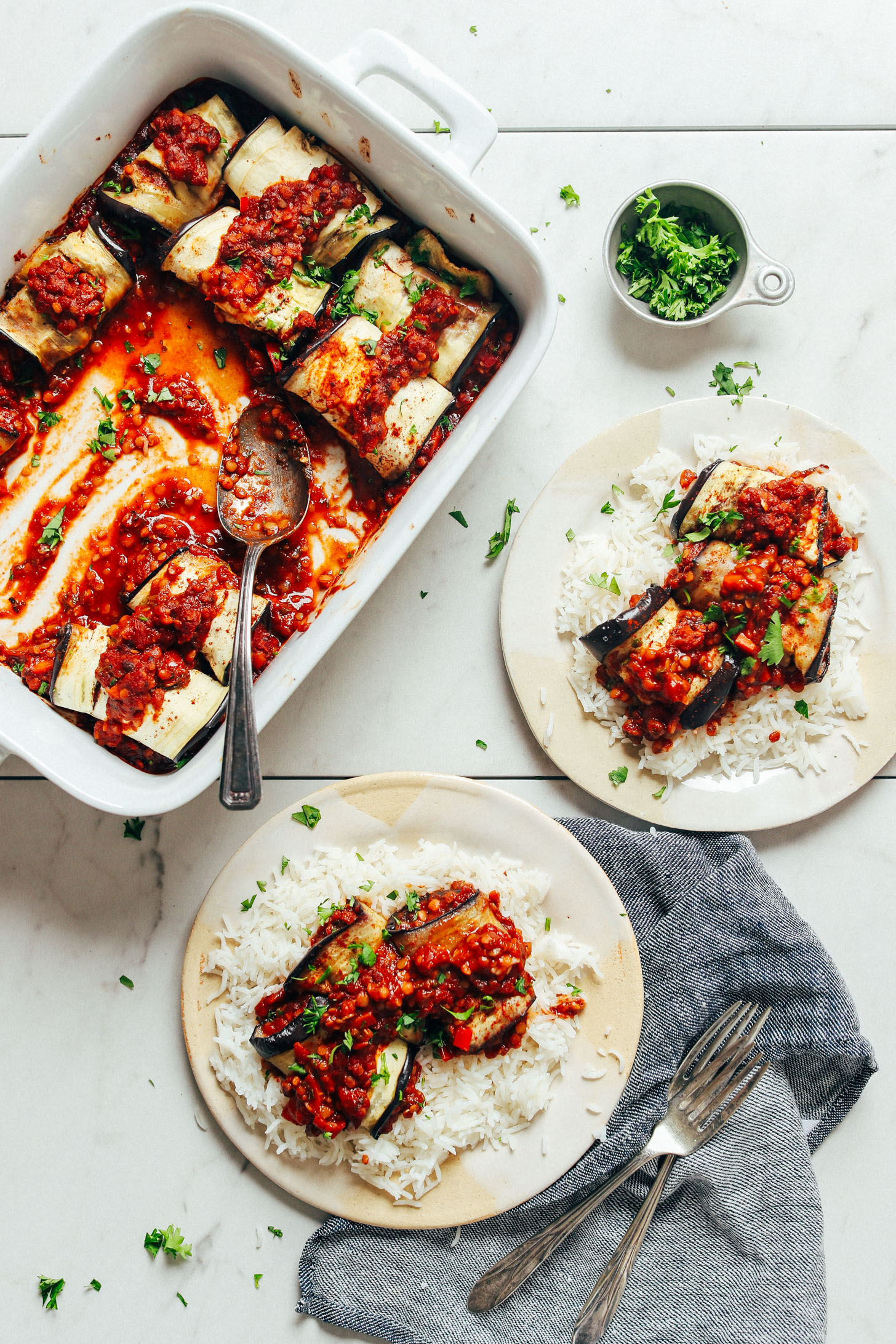 Eggplant rolls in a baking dish and on dinner plates over a bed of rice