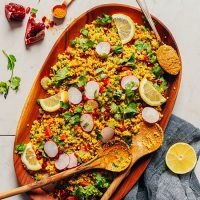Curried Quinoa Salad garnished with lemon slices and fresh herbs on wooden serving platter with wooden serving spoons
