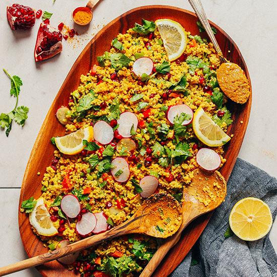 Curried Quinoa Salad garnished with lemon slices and fresh herbs on wooden serving platter with wooden serving spoons