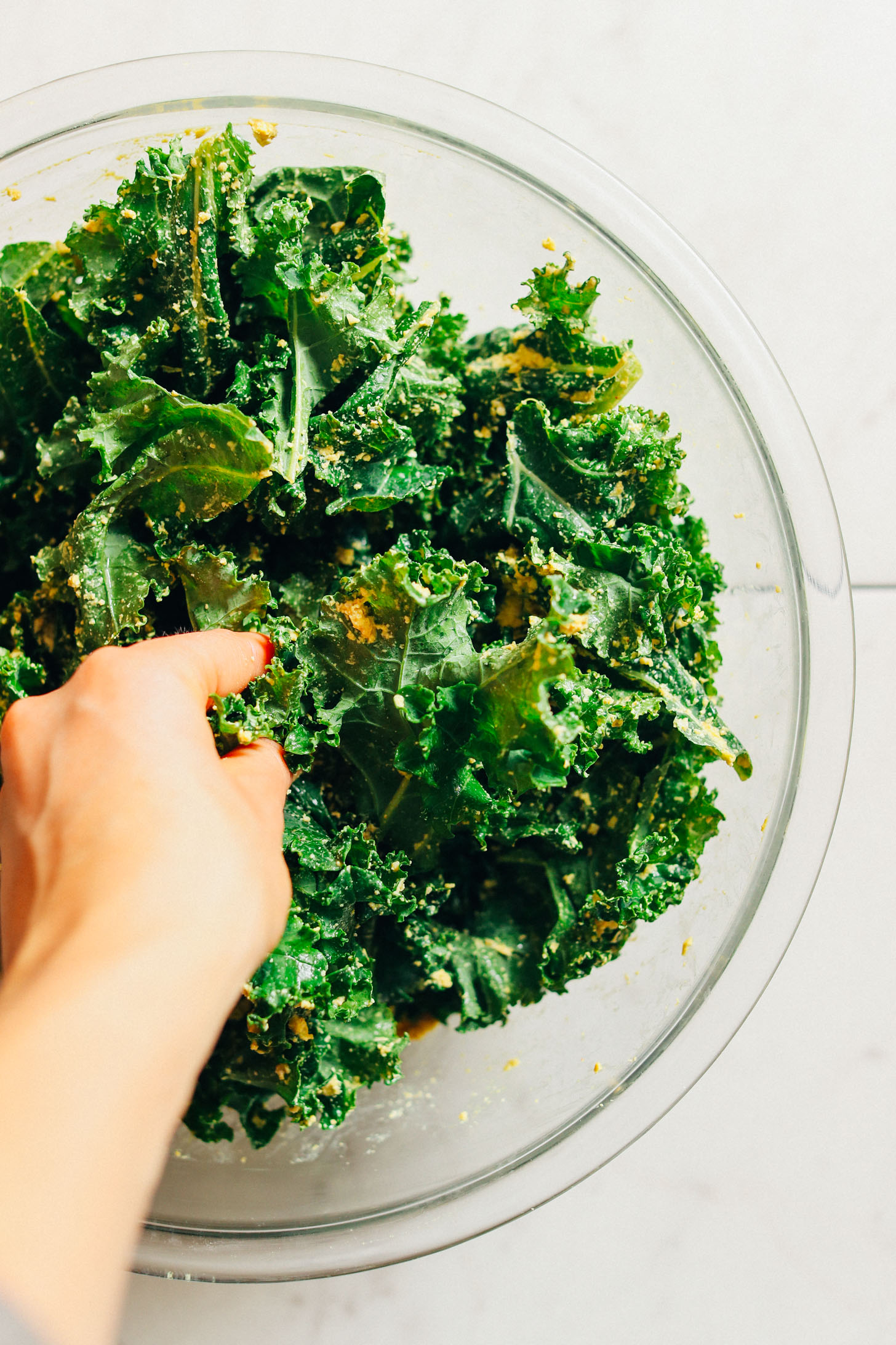 Using hands to toss kale leaves evenly with Sunflower Seed Cheeze
