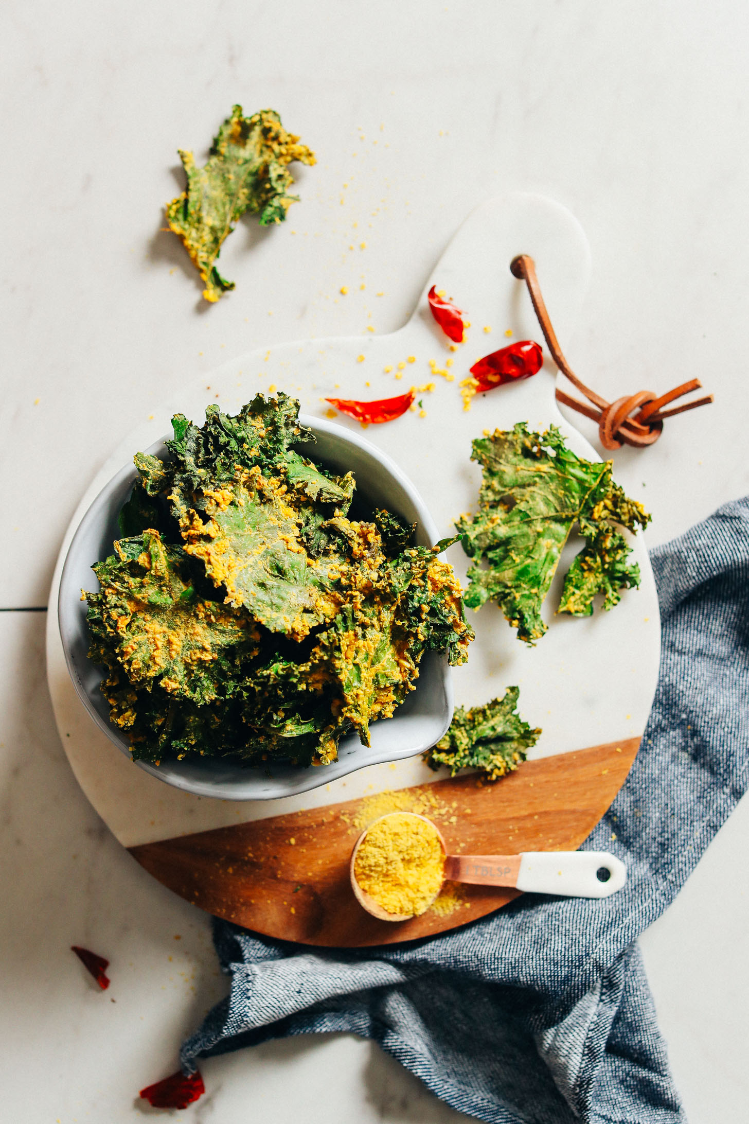 Marble cutting board with a bowl full of Crispy Baked Kale Chips for the perfect plant-based snack