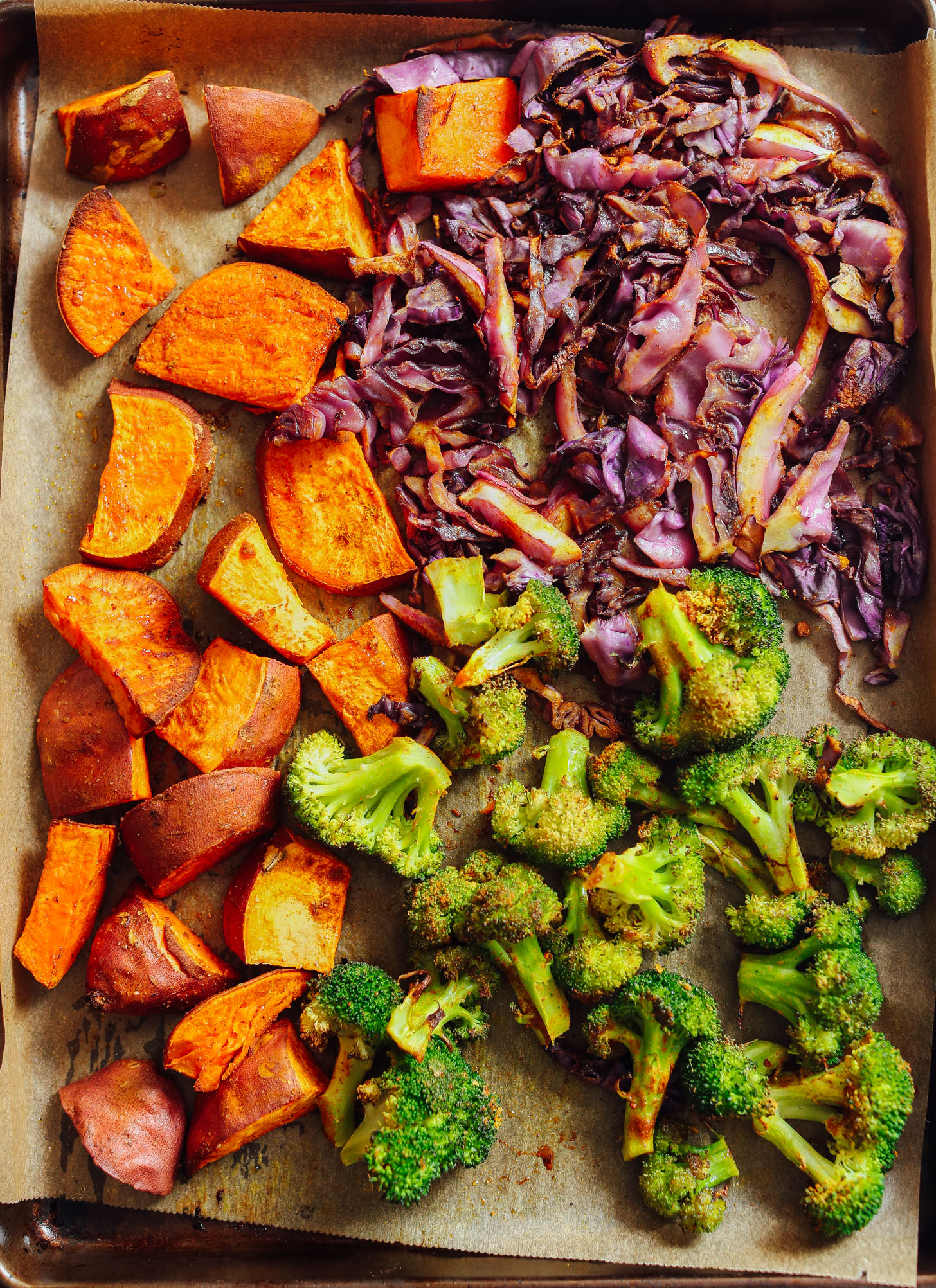 Freshly roasted sweet potatoes, broccoli, and cabbage on a parchment-lined baking sheet
