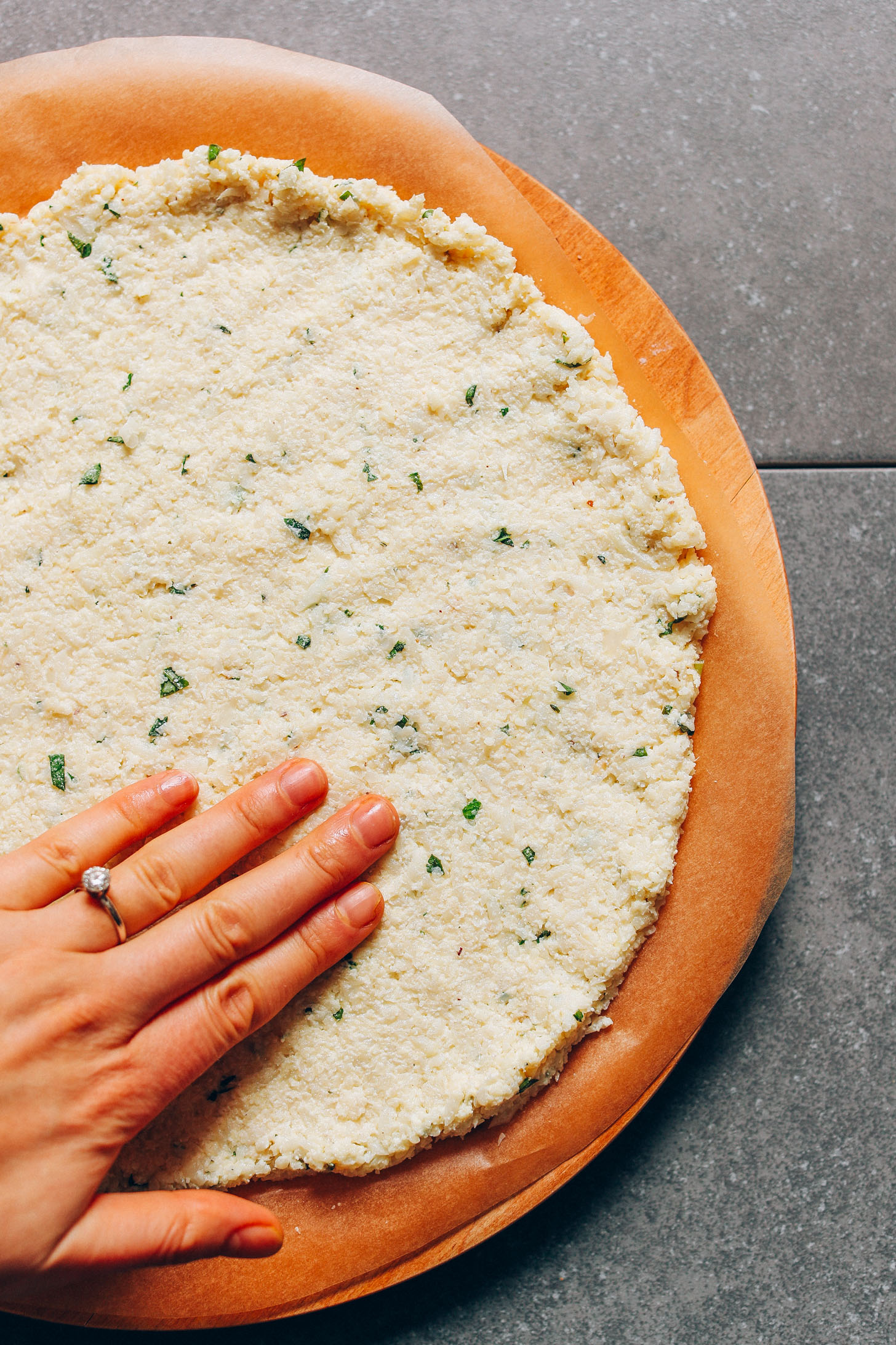 Pressing on a cauliflower pizza crust to flatten it