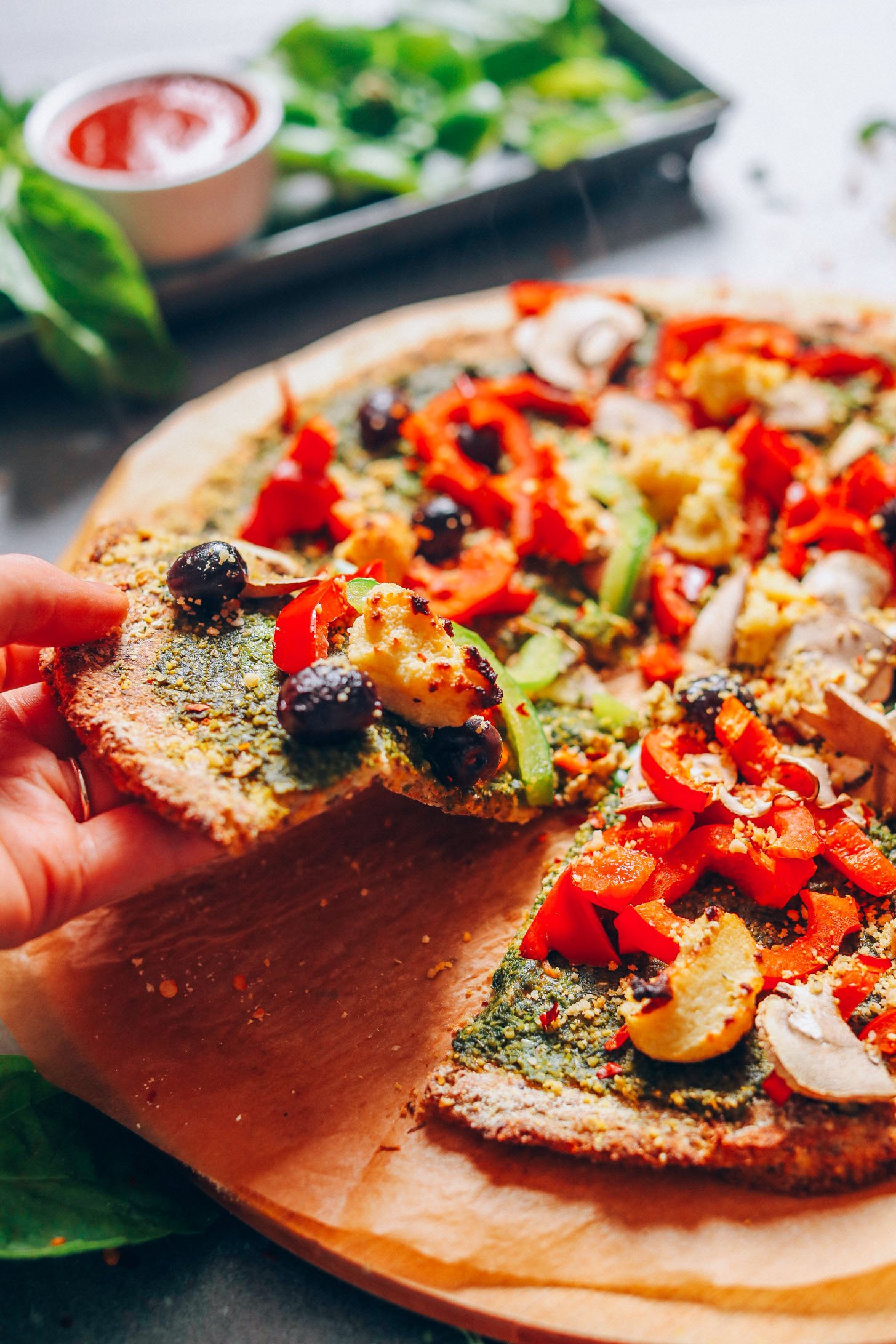 Picking up a slice of vegan pizza made with olives, peppers, and macadamia cheese