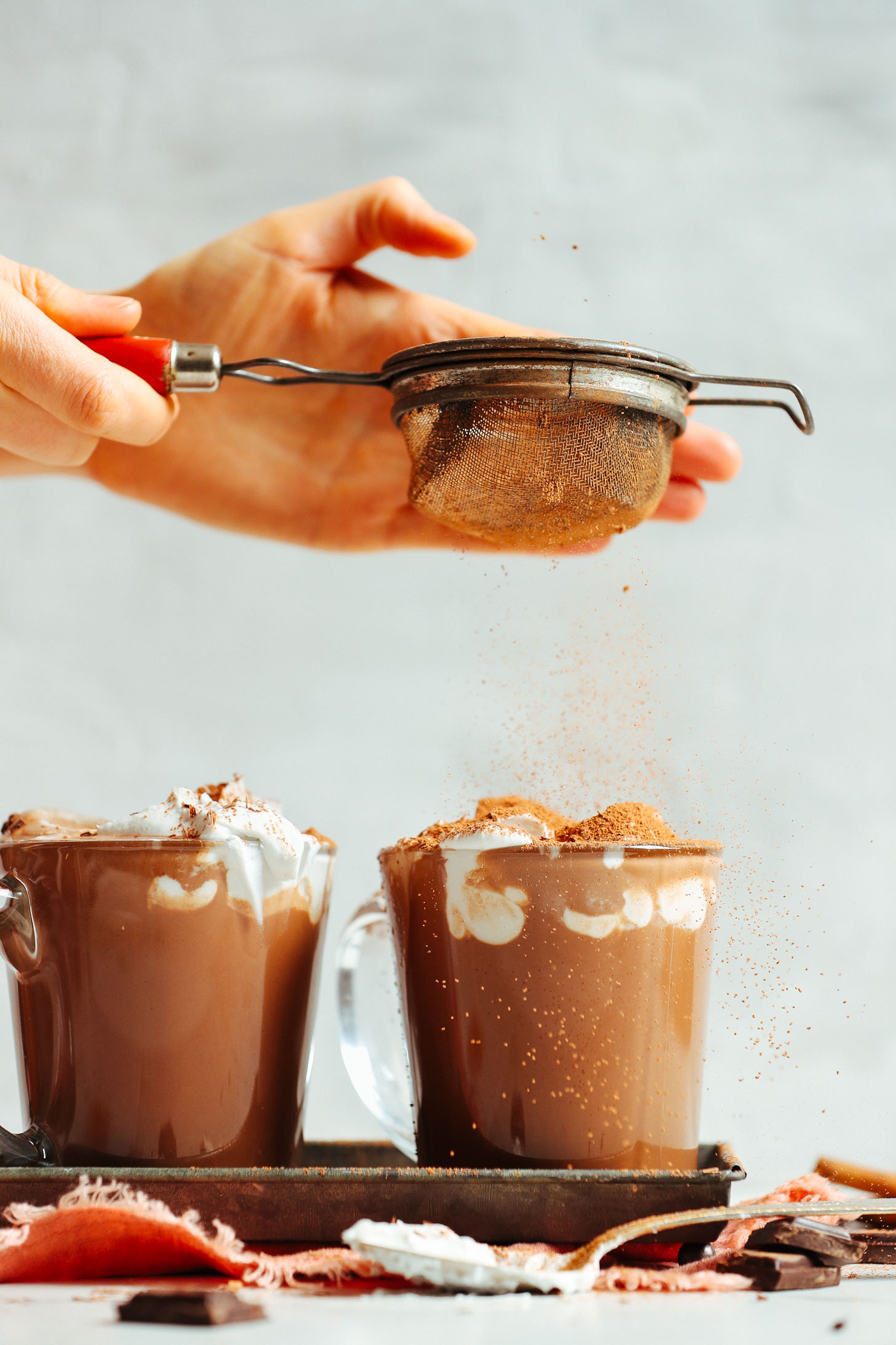 Sprinkling sifted cocoa powder onto the coconut whipped cream layer of Feel Good Vegan Hot Chocolate