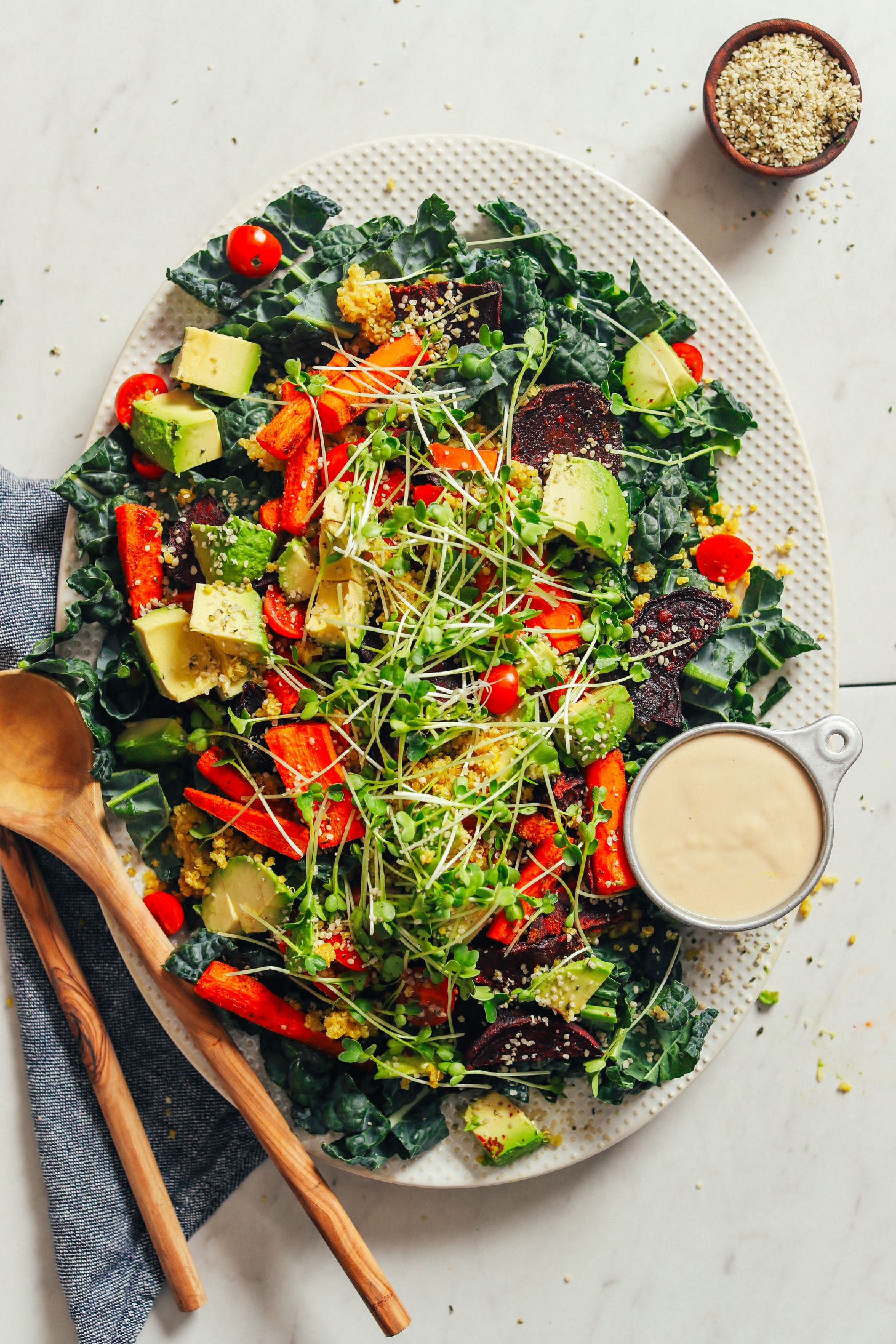 Large platter filled with vegan and gluten-free Loaded Kale Salad with sides of extra hemp seeds and tahini dressing
