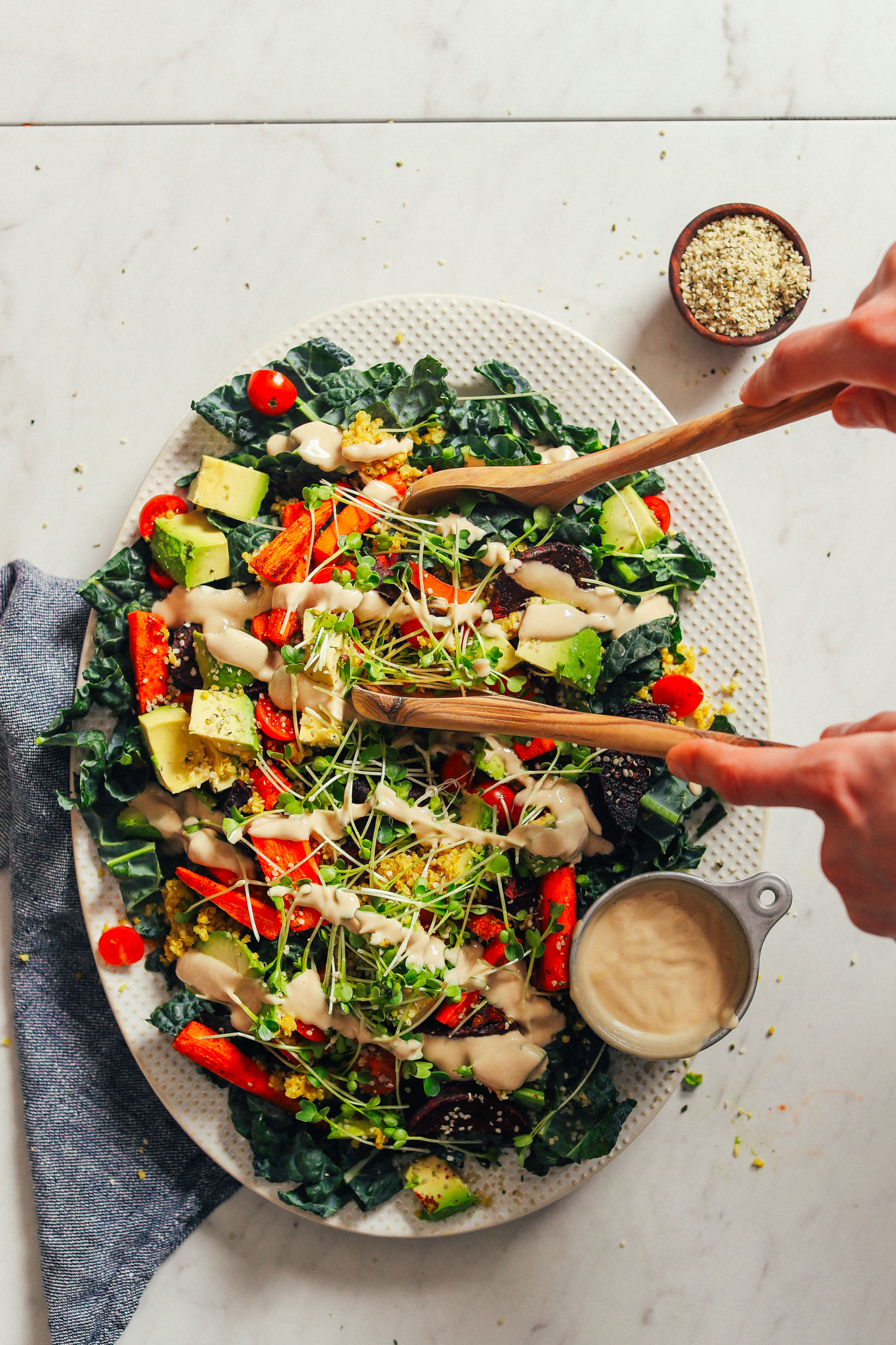 Big white serving platter with colorful, healthy Loaded Kale Salad with a side of hemp seeds and tahini dressing