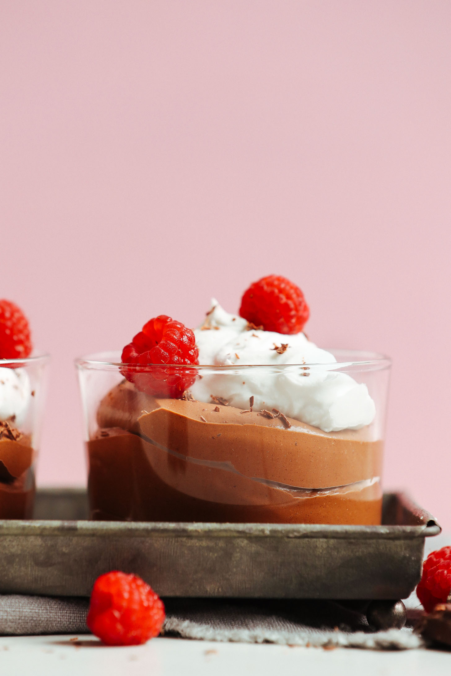 Close up shot of a glass of Naturally Sweetened Vegan Chocolate Mousse topped with coconut whipped cream and fresh raspberries