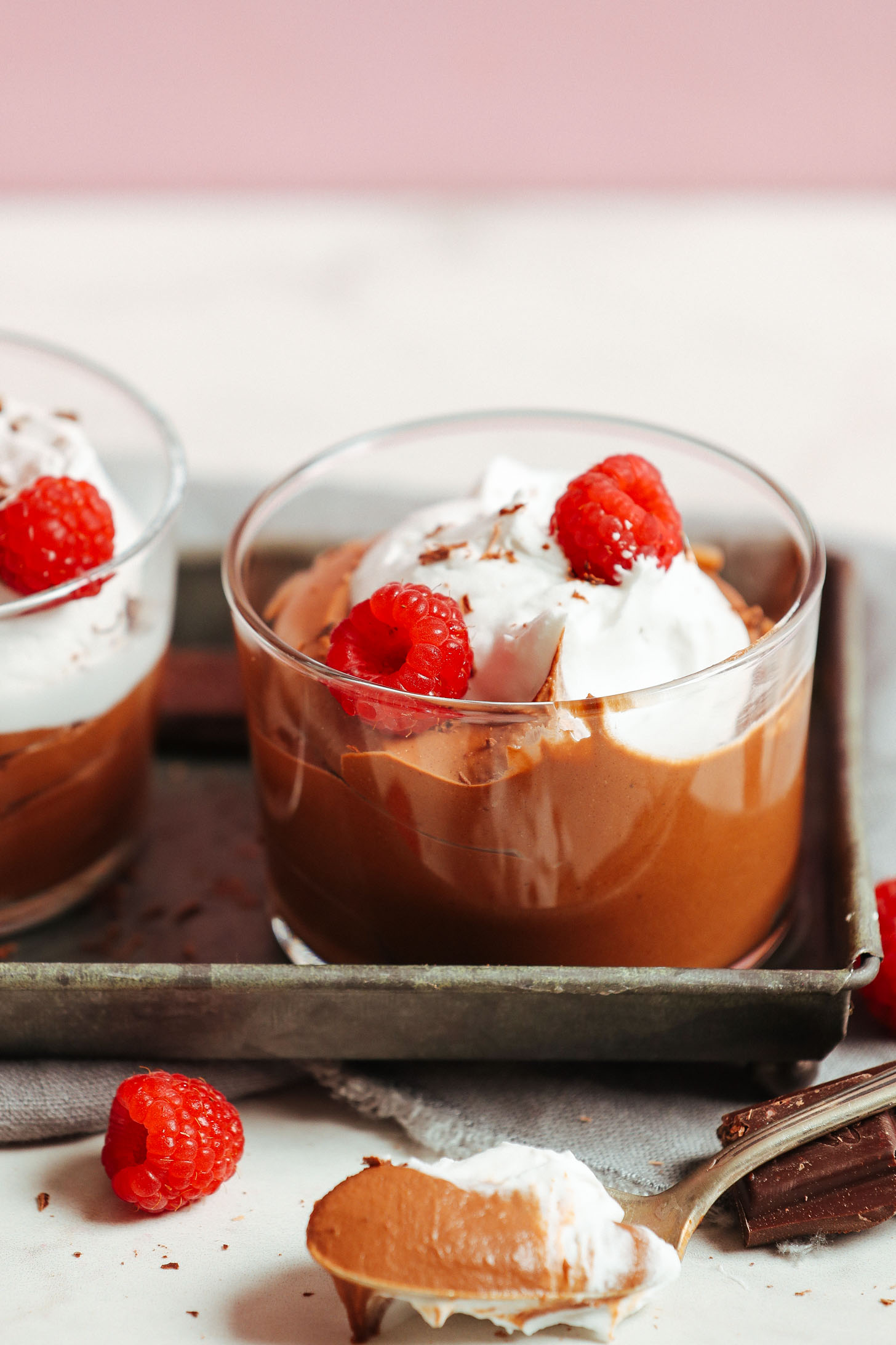 Close up shot of a glass of Naturally Sweetened Vegan Chocolate Mousse topped with coconut whipped cream and fresh raspberries