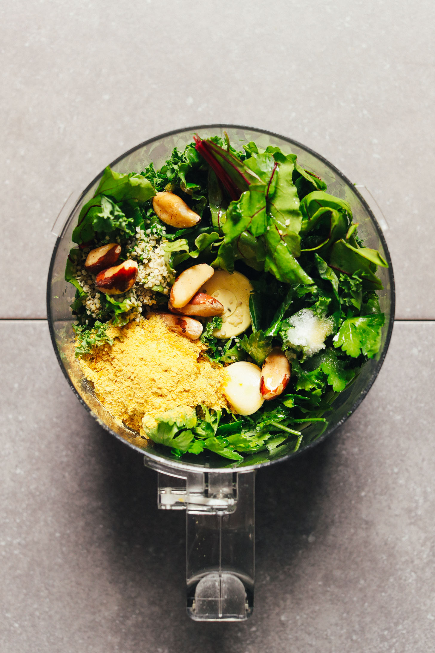 Food processor filled with ingredients for making our gluten-free Super-Green Vegan Pesto