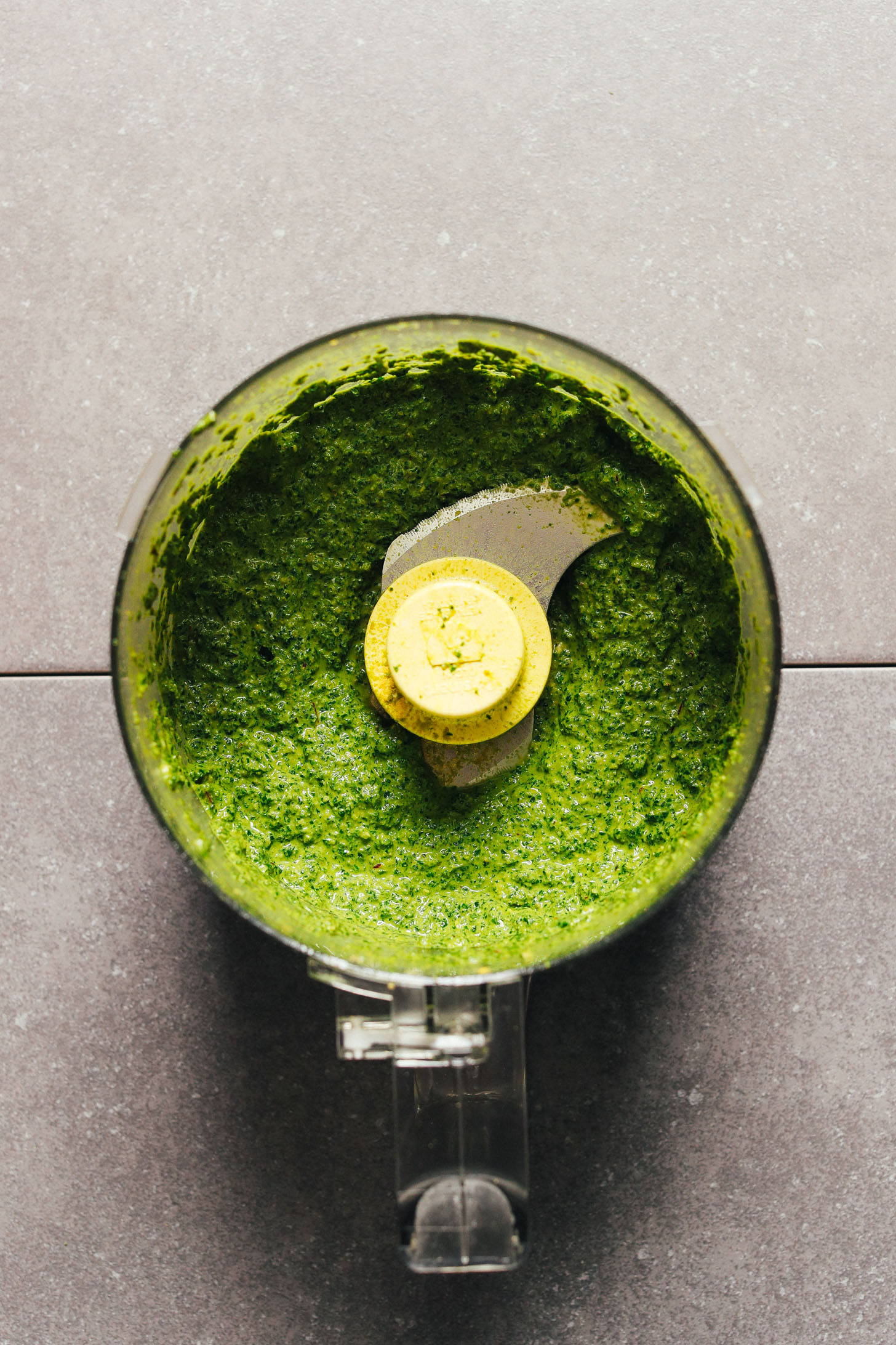 Food processor with freshly pulsed pesto made with vegan and gluten-free ingredients