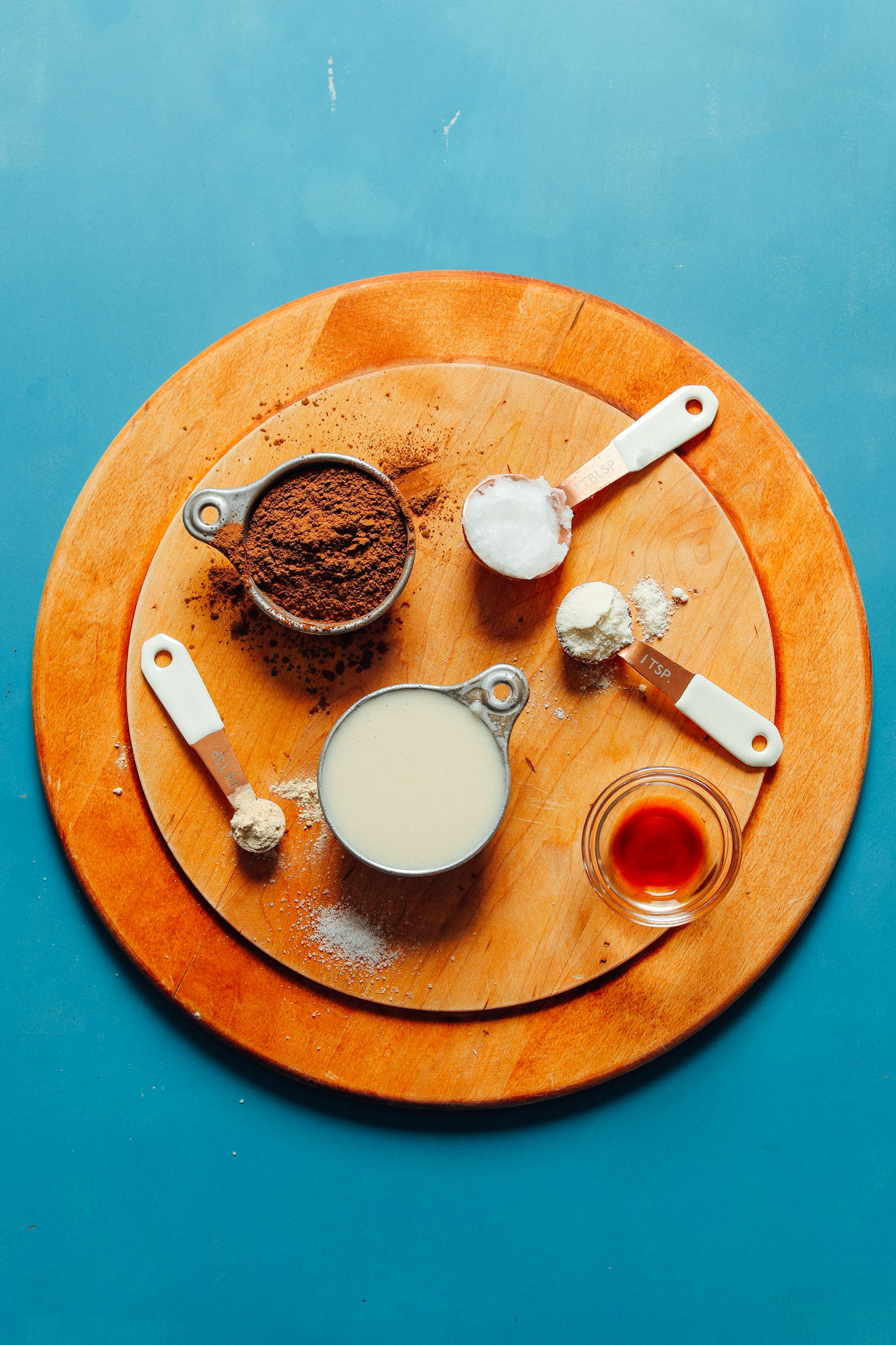 Coconut butter, coconut oil, toasted carob powder, maca, coconut flour, and vanilla on a wood cutting board ready to be made into Sugar-Free Coconut Carob Bars
