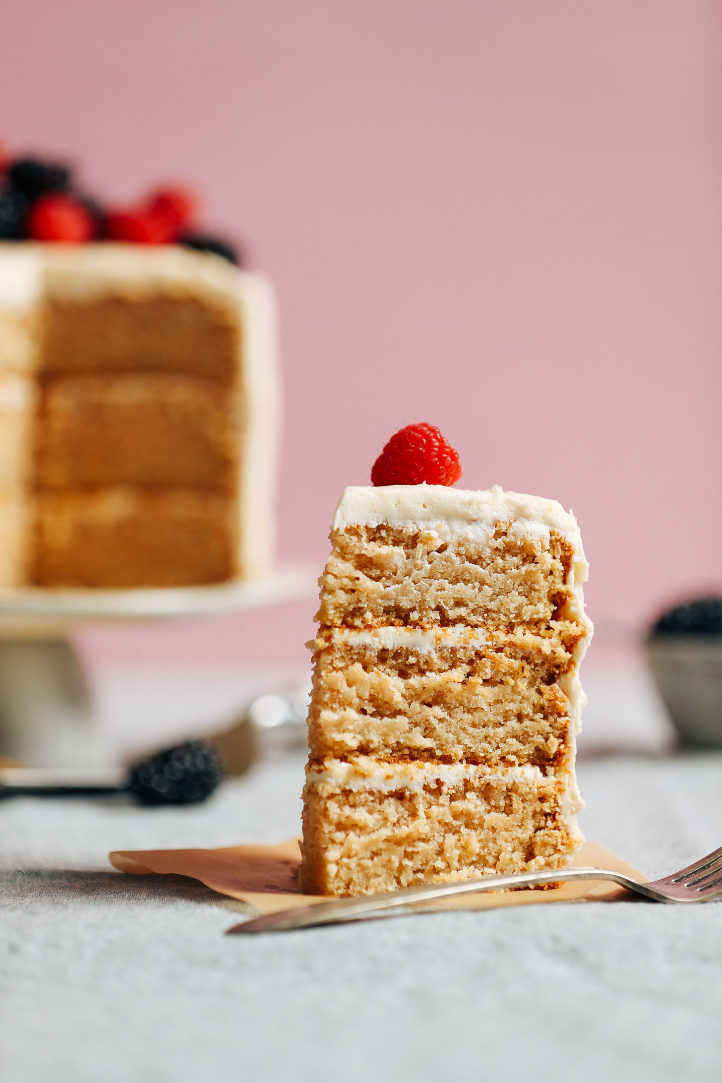 A slice of our fluffy and perfectly sweet 1-Bowl Vegan Gluten-Free Vanilla Cake topped with a fresh raspberry