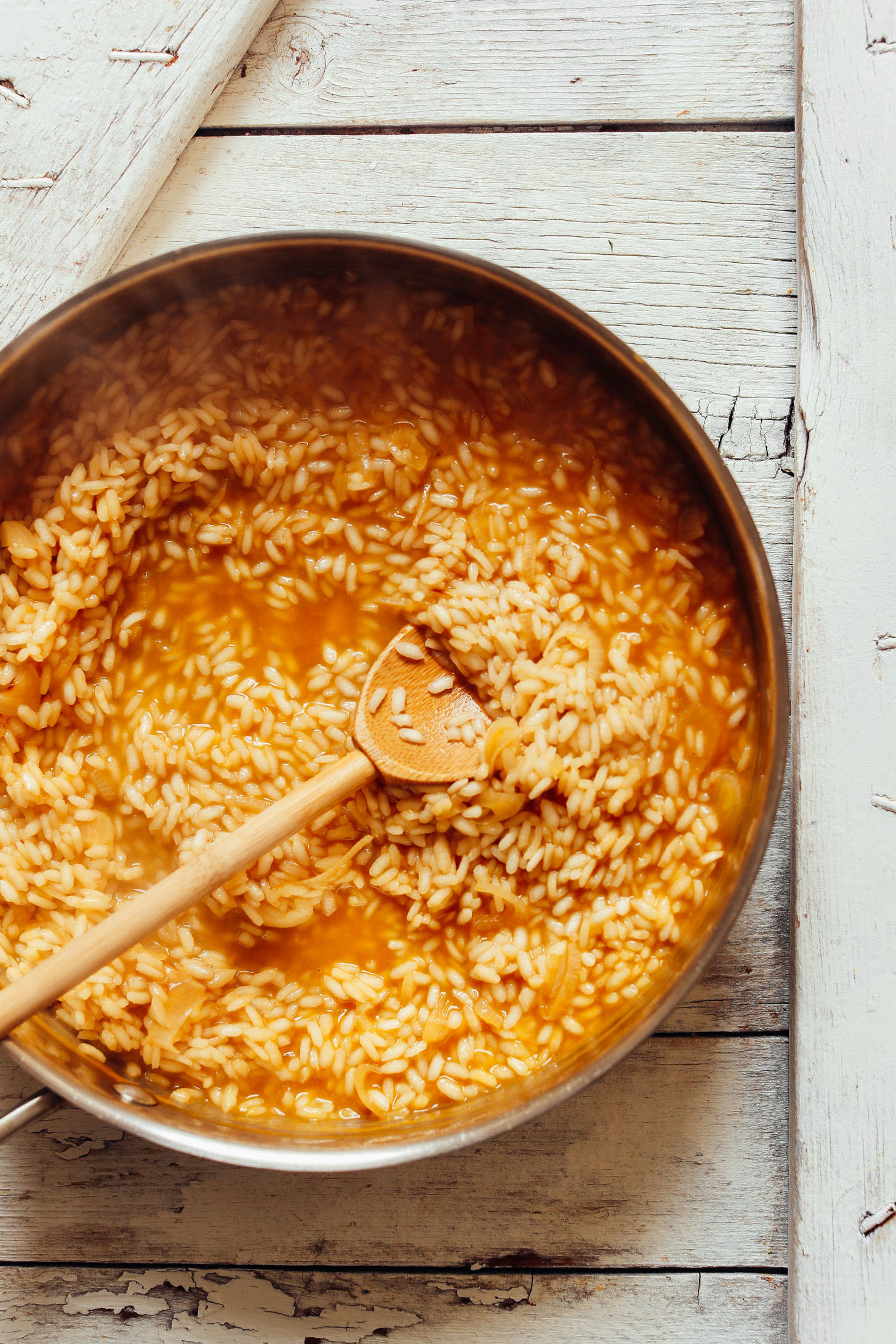 Using a wooden spoon to stir together arborio rice and vegetable broth for this vegan Creamy Vegetable Risotto