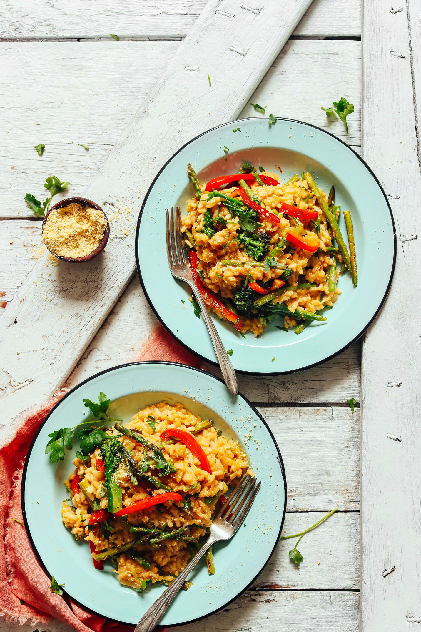 Two hearty servings of Creamy Vegetable Risotto in dinner bowls with a side of vegan parmesan
