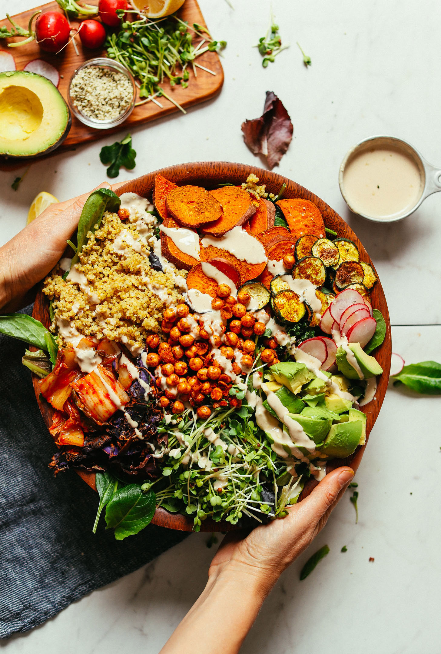 Large salad serving bowl with fresh greens, vegetables, chickpeas, and savory tahini dressing