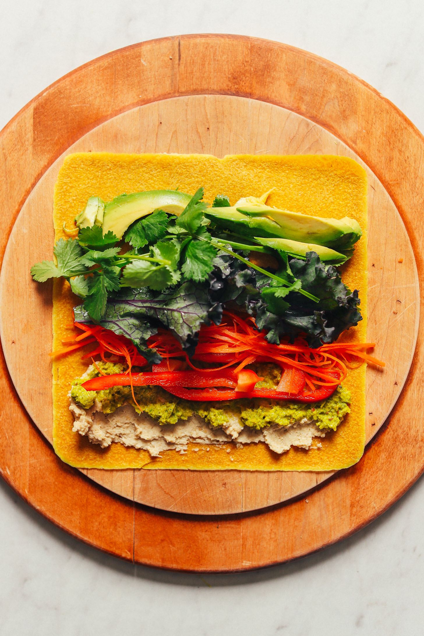Coconut wrap displayed open on a cutting board loaded with vegetables, hummus, and green curry paste 