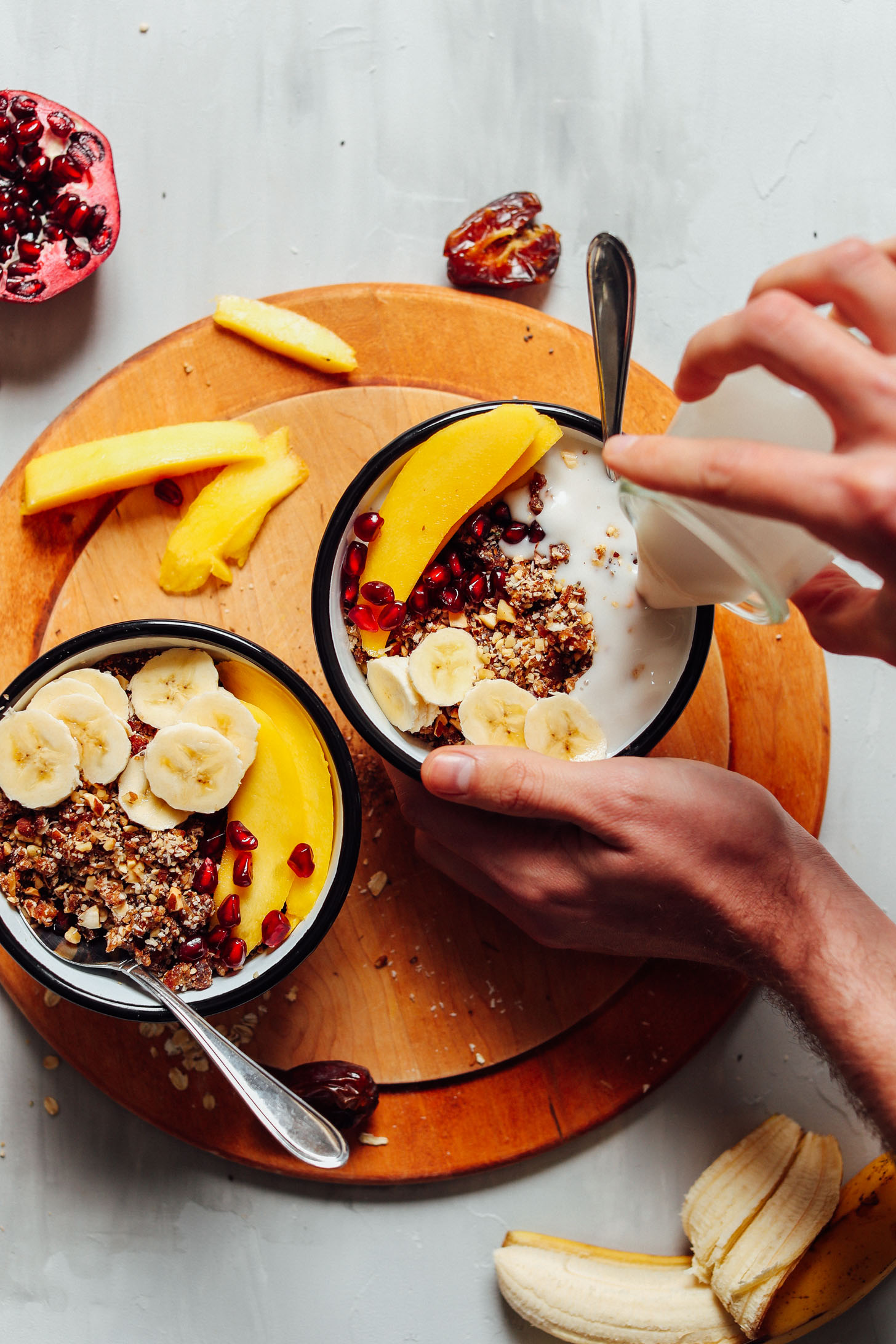 Pouring coconut milk into a bowl of gluten-free vegan granola with fresh fruit