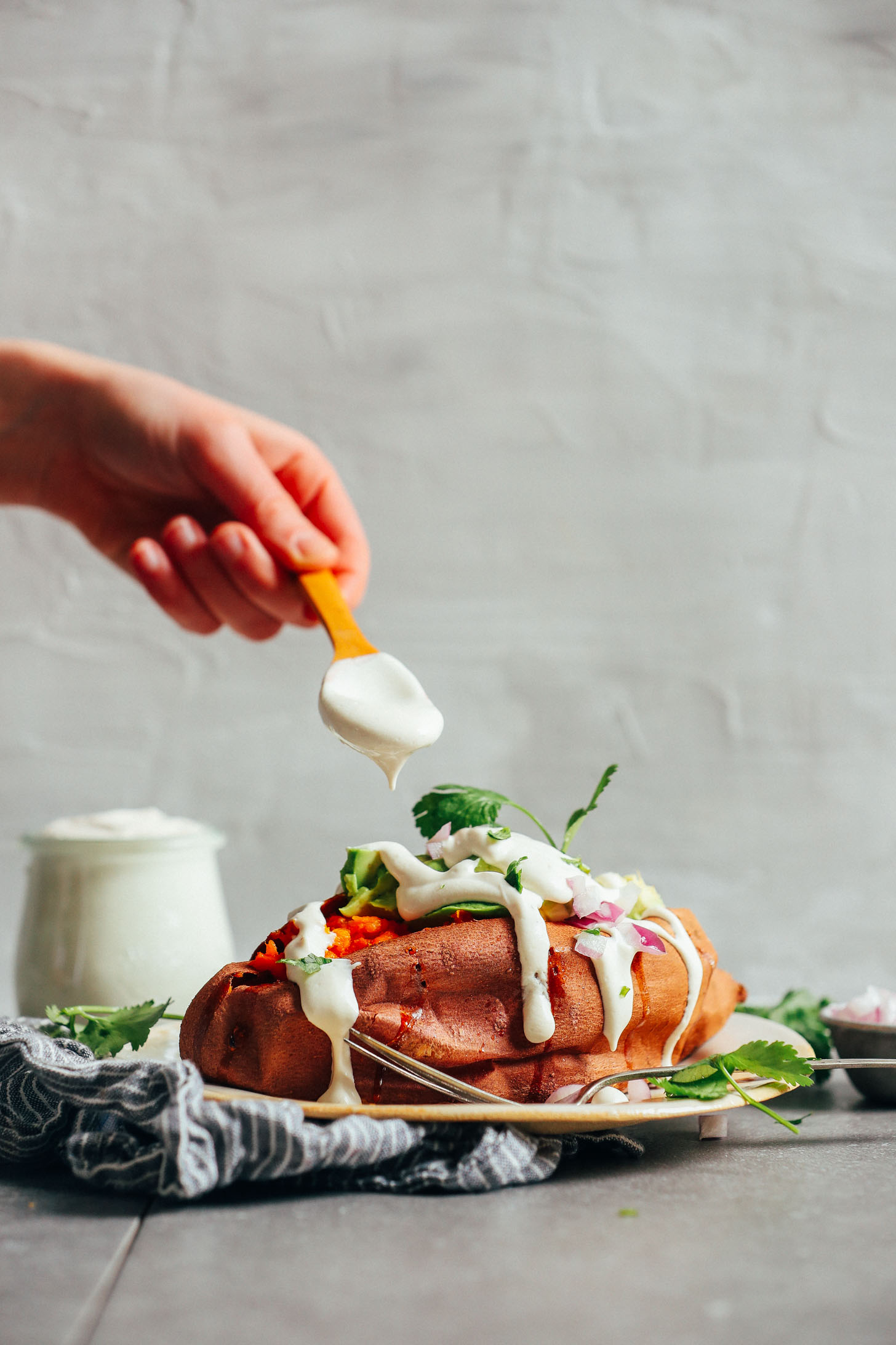 Drizzling Vegan Sour Cream onto a loaded sweet potato for a delicious plant-based meal