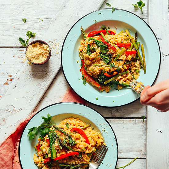 Two plates of Creamy Vegetable Risotto beside a small bowl of vegan parmesan cheese