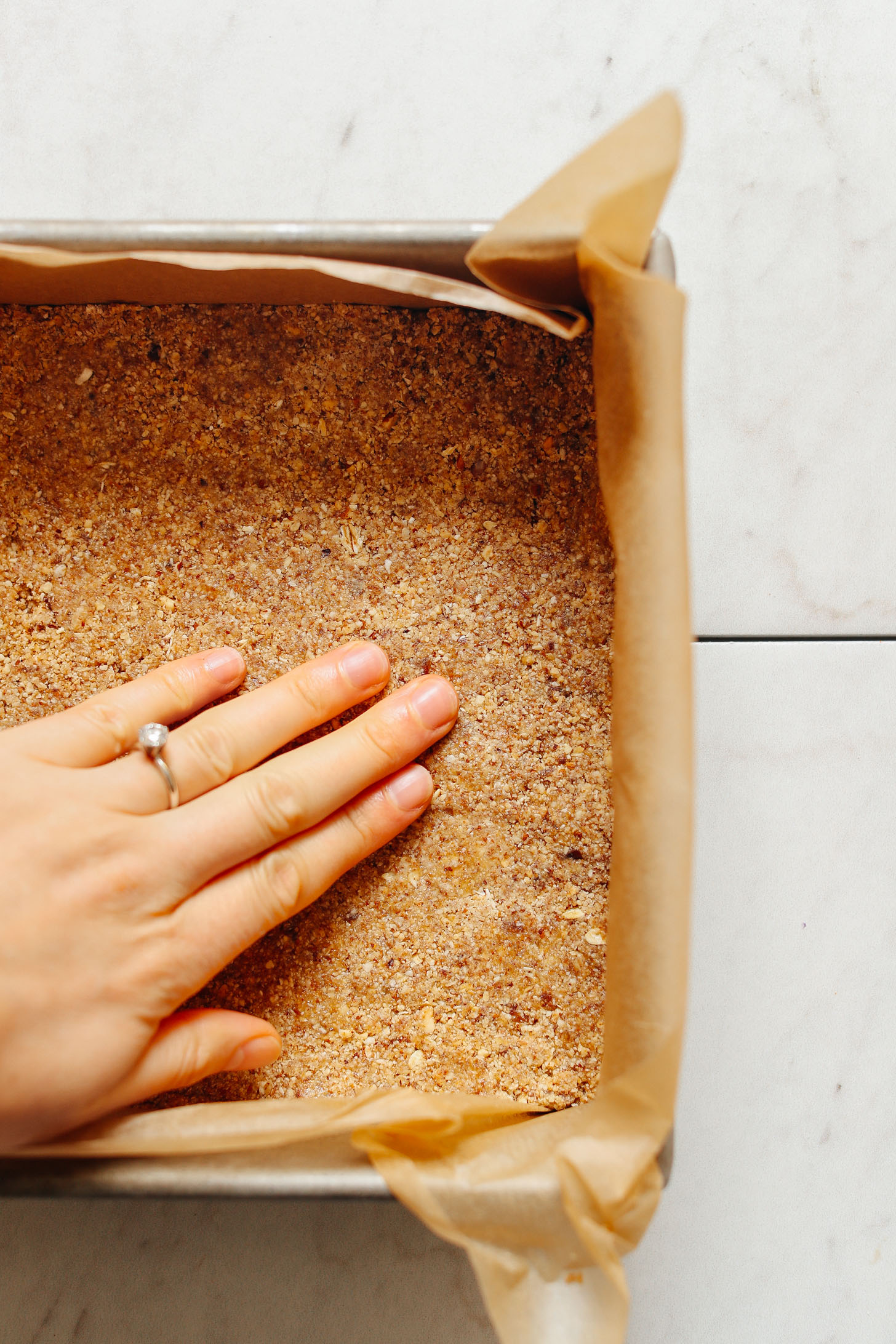 Parchment-lined metal baking pan with crust layer for these Vegan 7-Layer Bars