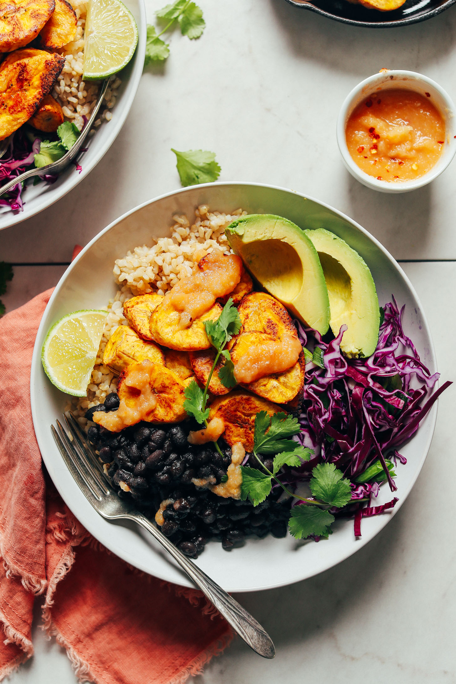 Hearty serving of Black Bean Plantain Bowls full of flavorful beans, rice, cabbage, avocado, plantains, cilantro, and hot sauce