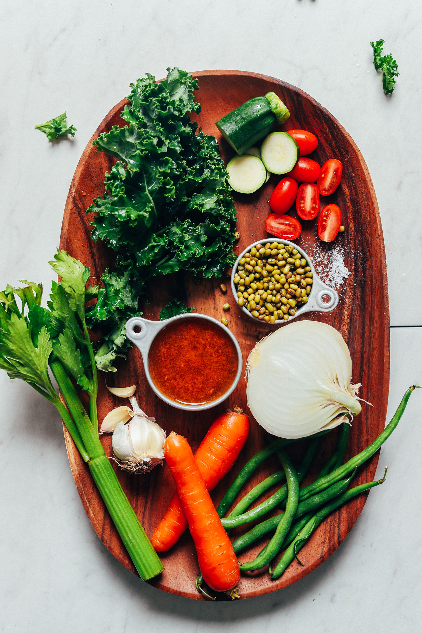 Platter of ingredients including onion, green beans, carrots, garlic, celery, diced tomatoes, mung beans, kale, zucchini, tomatoes, and salt