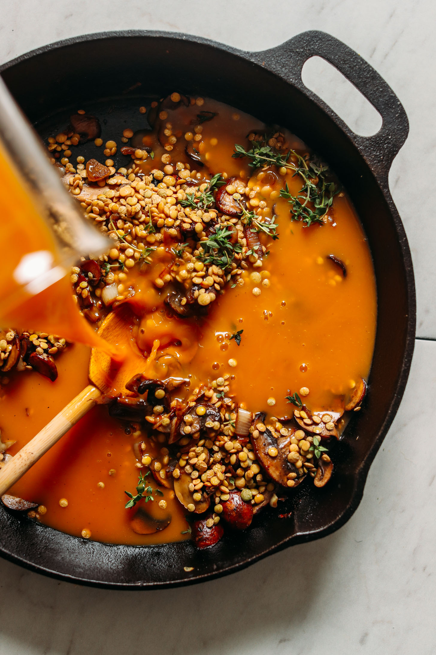 Pouring vegetable broth over lentils and veggies in a cast iron skillet to make gluten-free Lentil Mushroom Stew