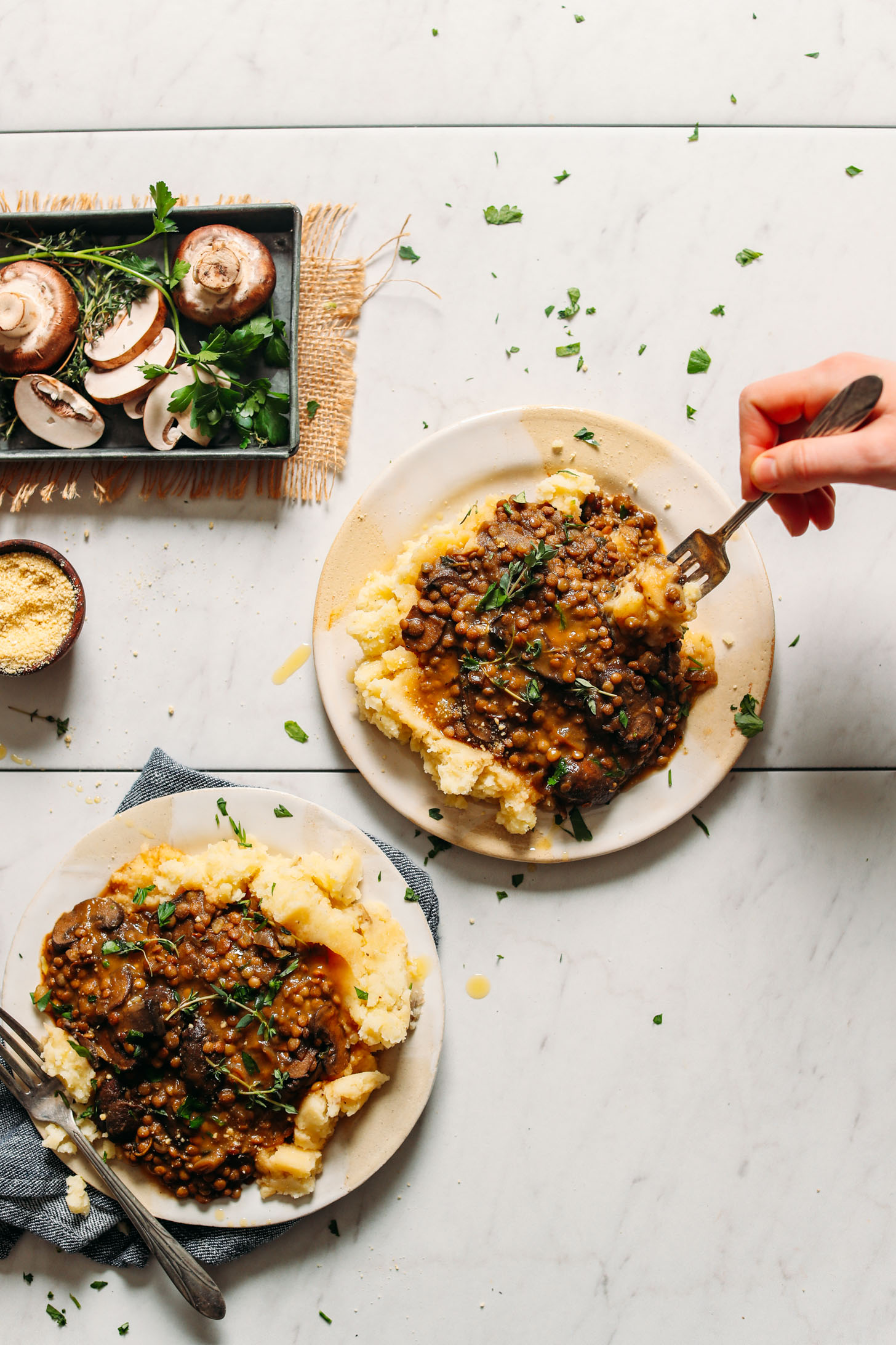 Two serving plates loaded with comforting vegan mashed potatoes topped with super hearty Lentil Mushroom Stew