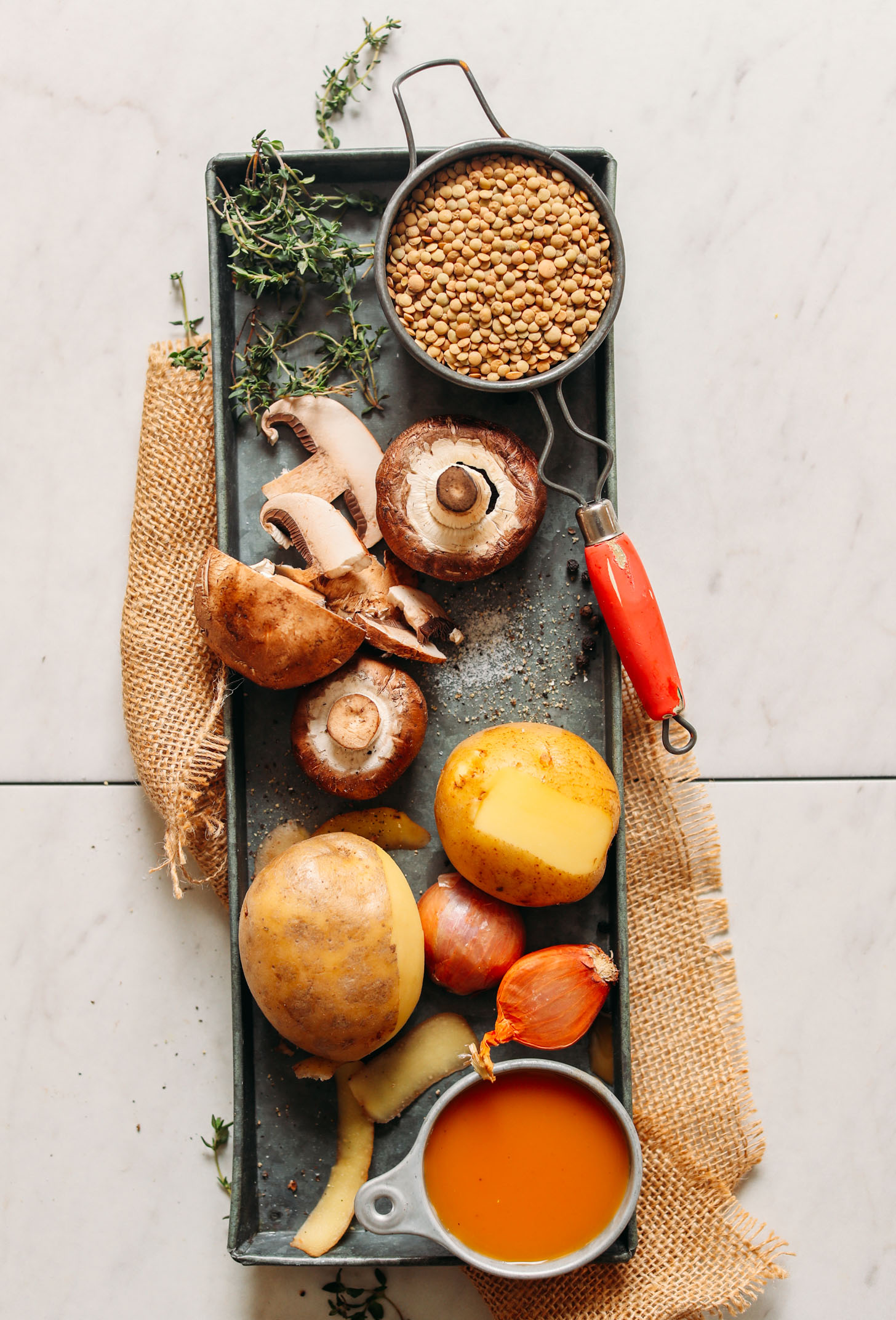 Metal serving tray filled with thyme, lentils, mushrooms, potatoes, shallots, and vegetable broth for making Lentil Mushroom Stew Over Mashed Potatoes