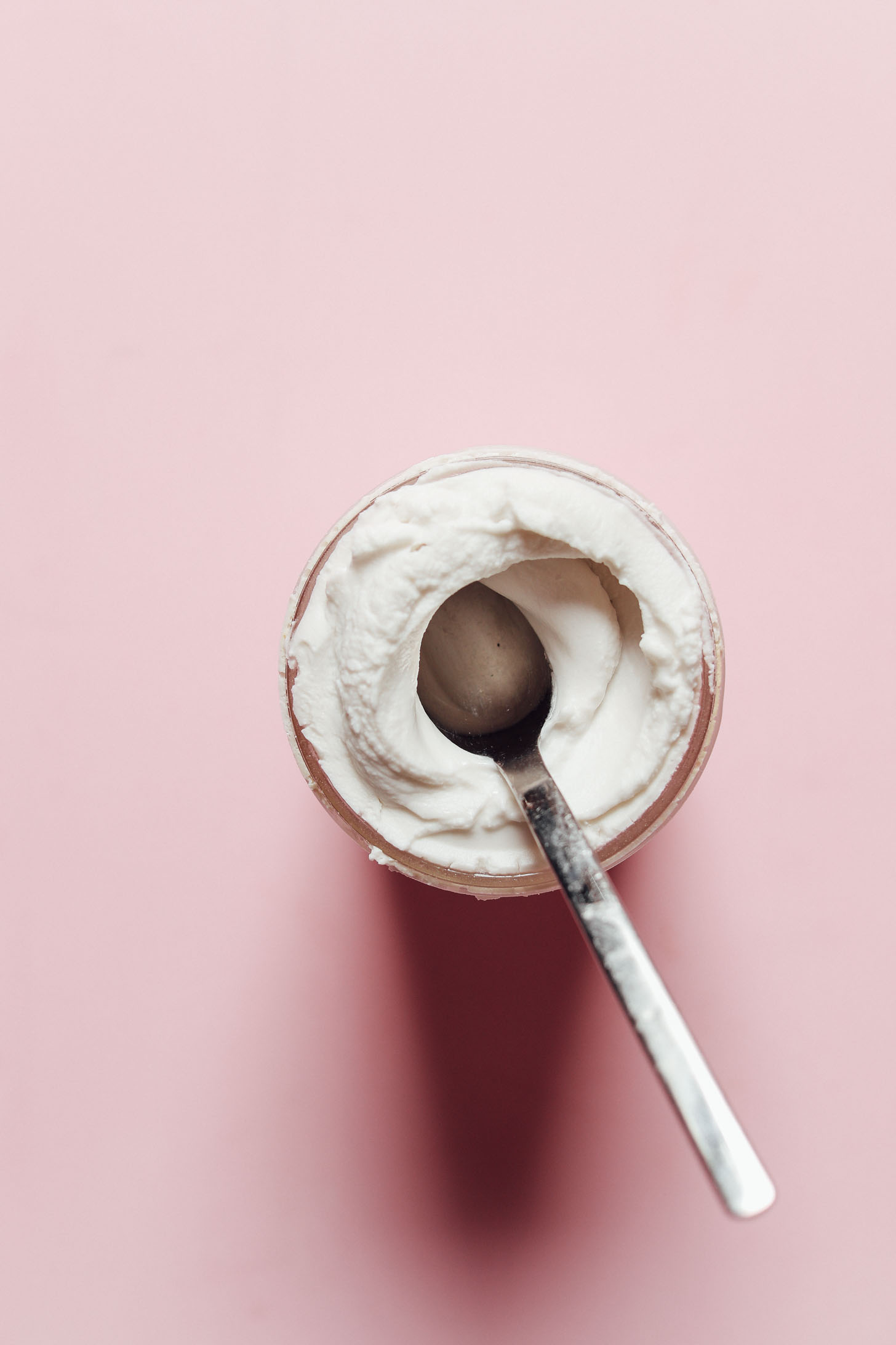 Spoon dipped into a glass jar of coconut yogurt for making rich and creamy Coconut Yogurt Cheesecake