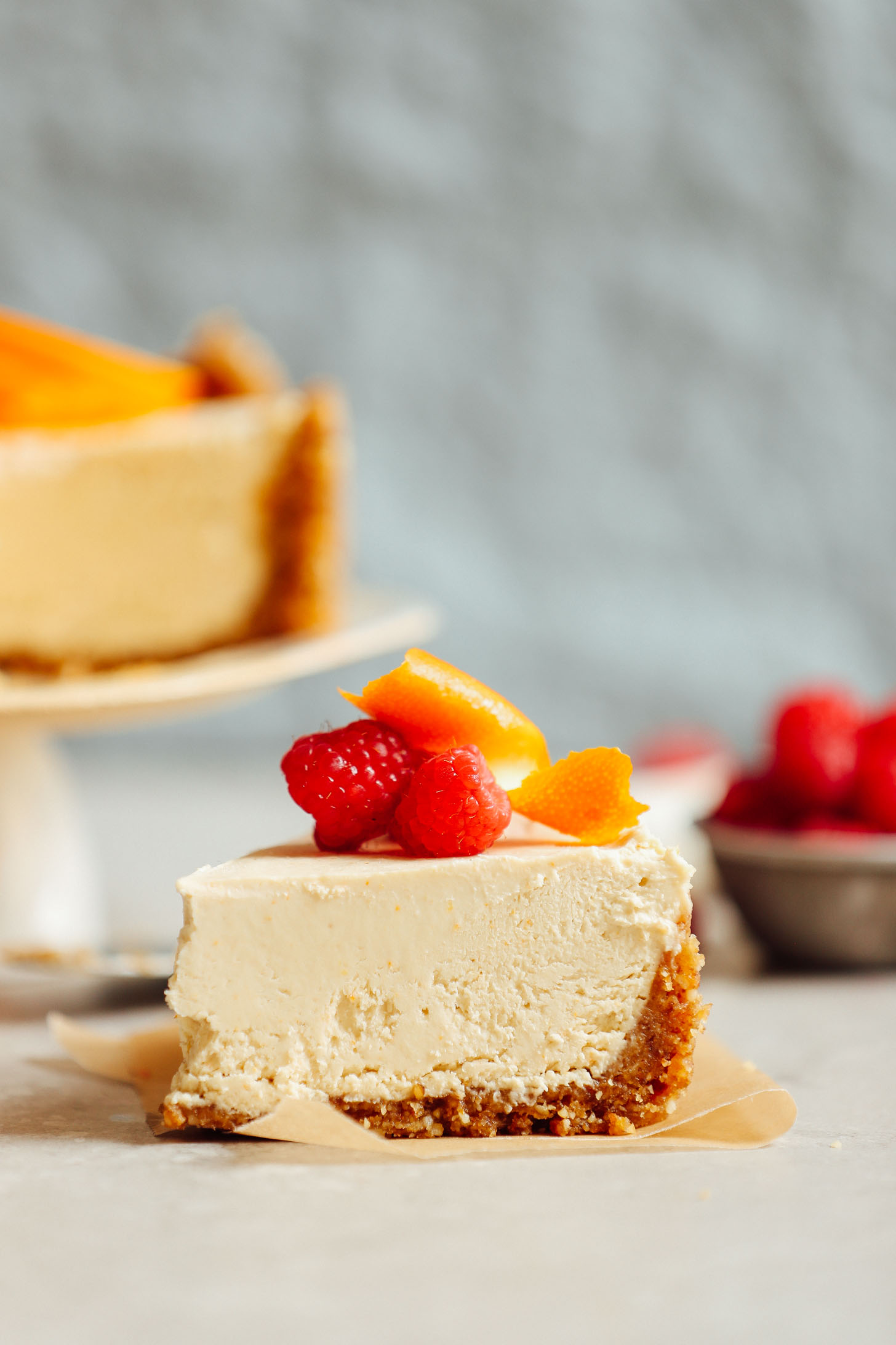 Close up shot of a slice of Coconut Yogurt Cheesecake topped with raspberries and orange slices
