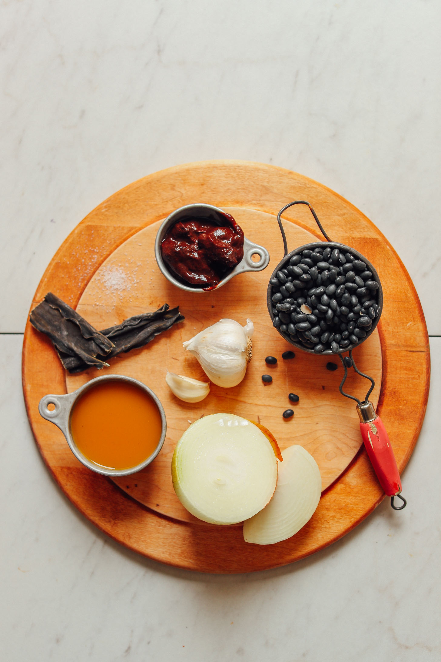 Wood platter displaying dry beans, onion, garlic, vegetable broth, adobo chiles, and kombu