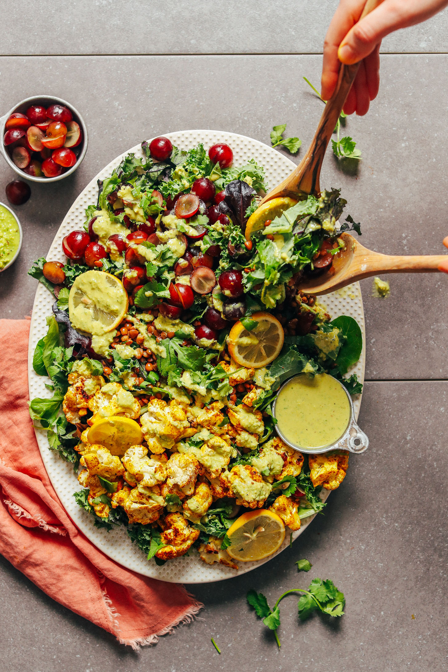 Using wooden spoons to scoop up a serving of this fresh and healthy Kale Salad with Grapes, Lentils, and Curry Roasted Cauliflower