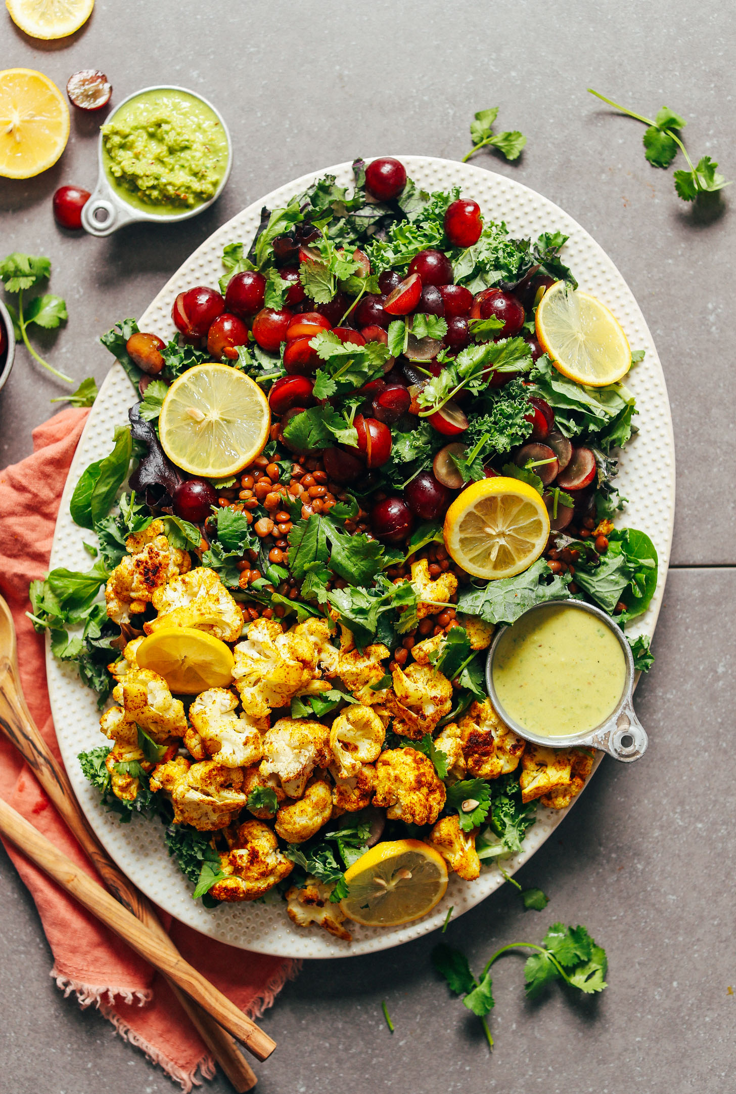 A large platter full of Kale Salad with Grapes, Lentils, Curry Roasted Cauliflower, and Green Curry Tahini Dressing