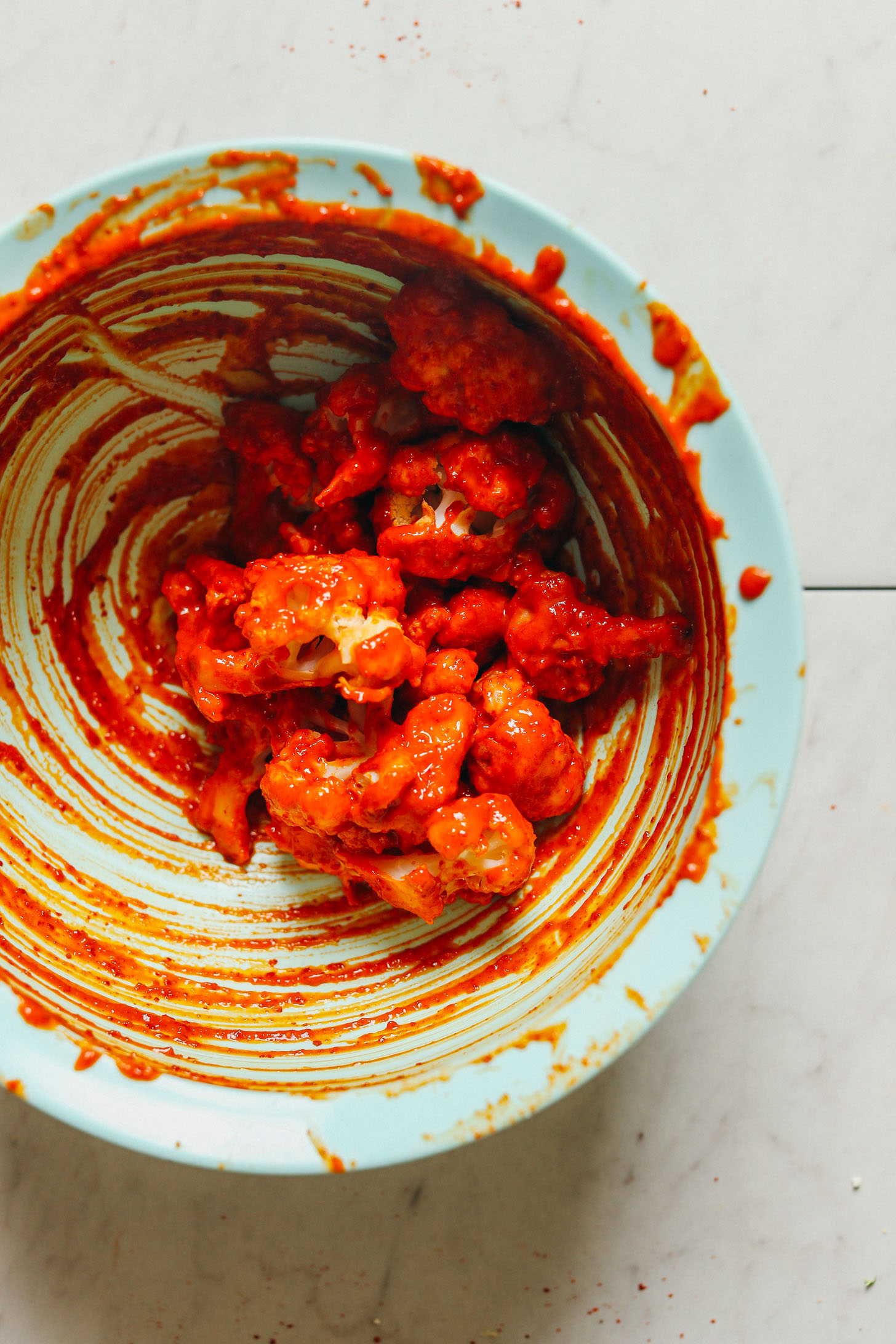 Mixing bowl with cauliflower coated in sauce for vegan gluten-free Korean-Spiced Cauliflower Wings