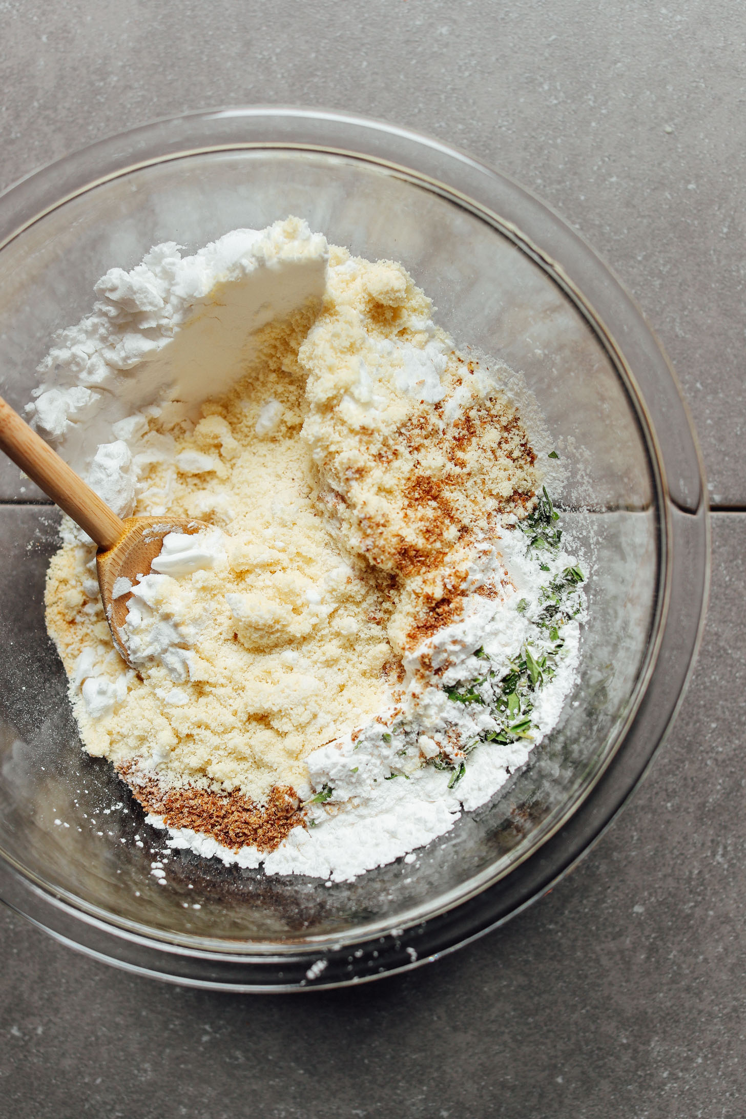Stirring together dry ingredients- almond flour, potato starch, arrowroot starch, flaxseed meal, baking soda, baking soda, and spices for Gluten-Free Vegan Pizza Crust