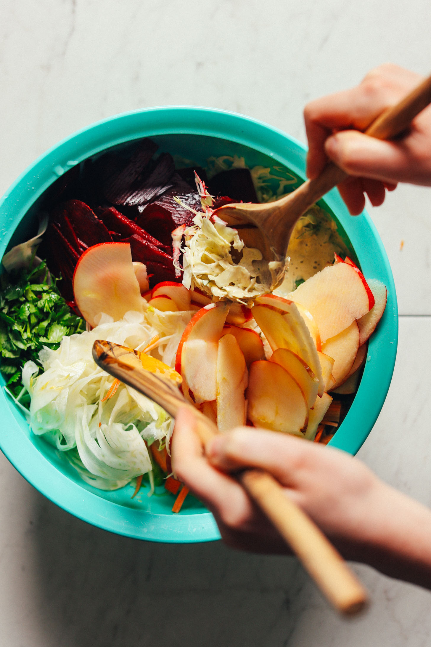 Using salad tongs to toss the fresh, crunchy vegetables of this Super Cleansing Slaw with the Rosemary Tahini Dressing