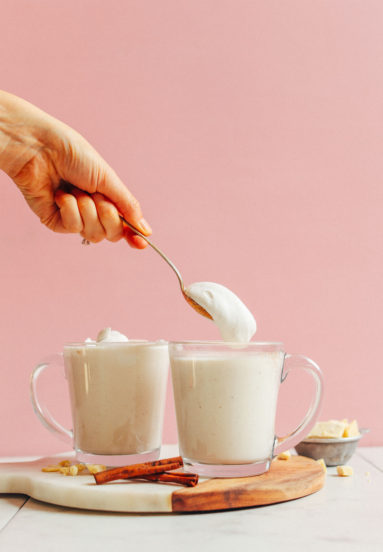 Scooping a spoonful of coconut whipped cream onto Vegan White Hot Chocolate for dessert