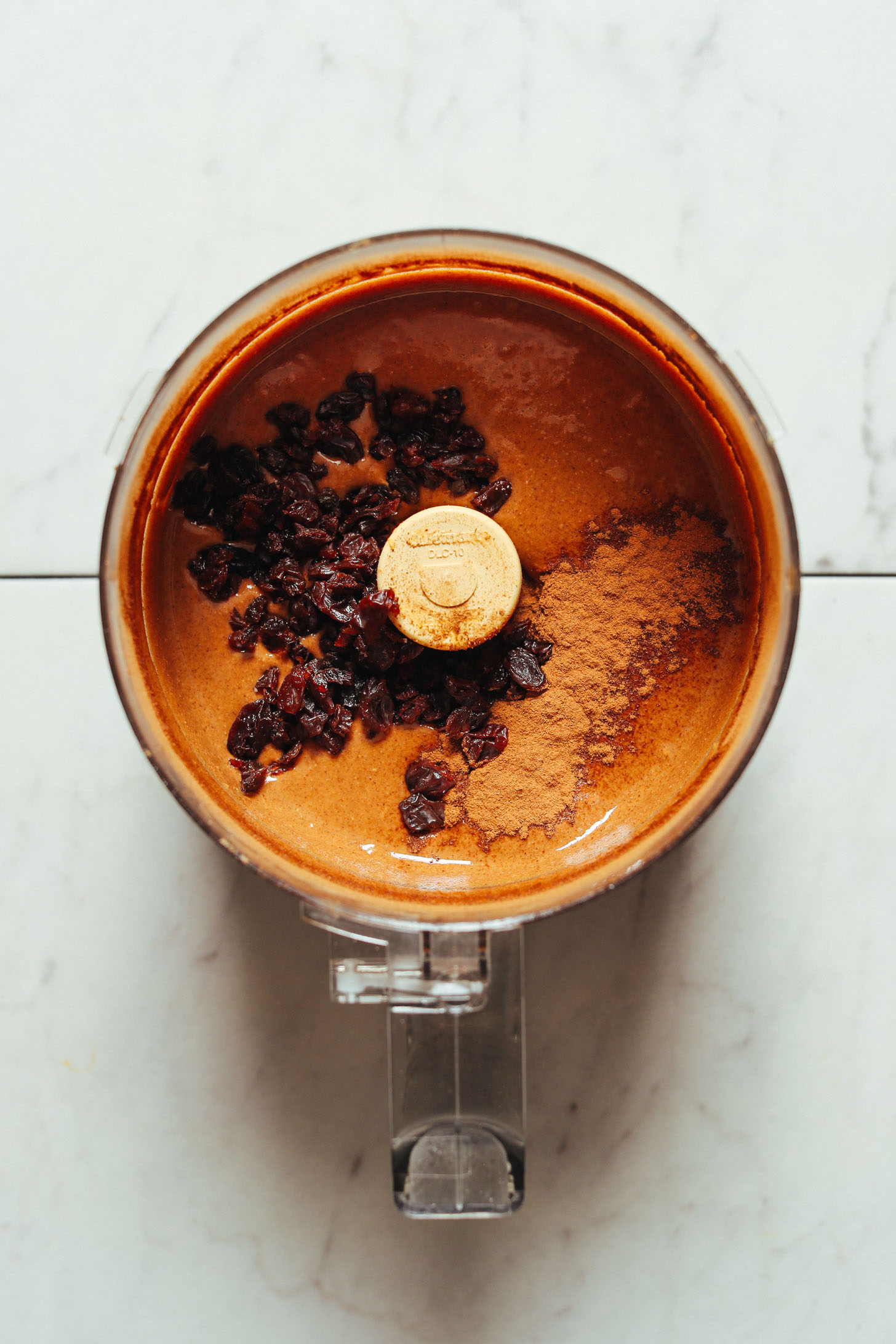 Food processor filled with smooth homemade peanut butter, raisins, and cinnamon