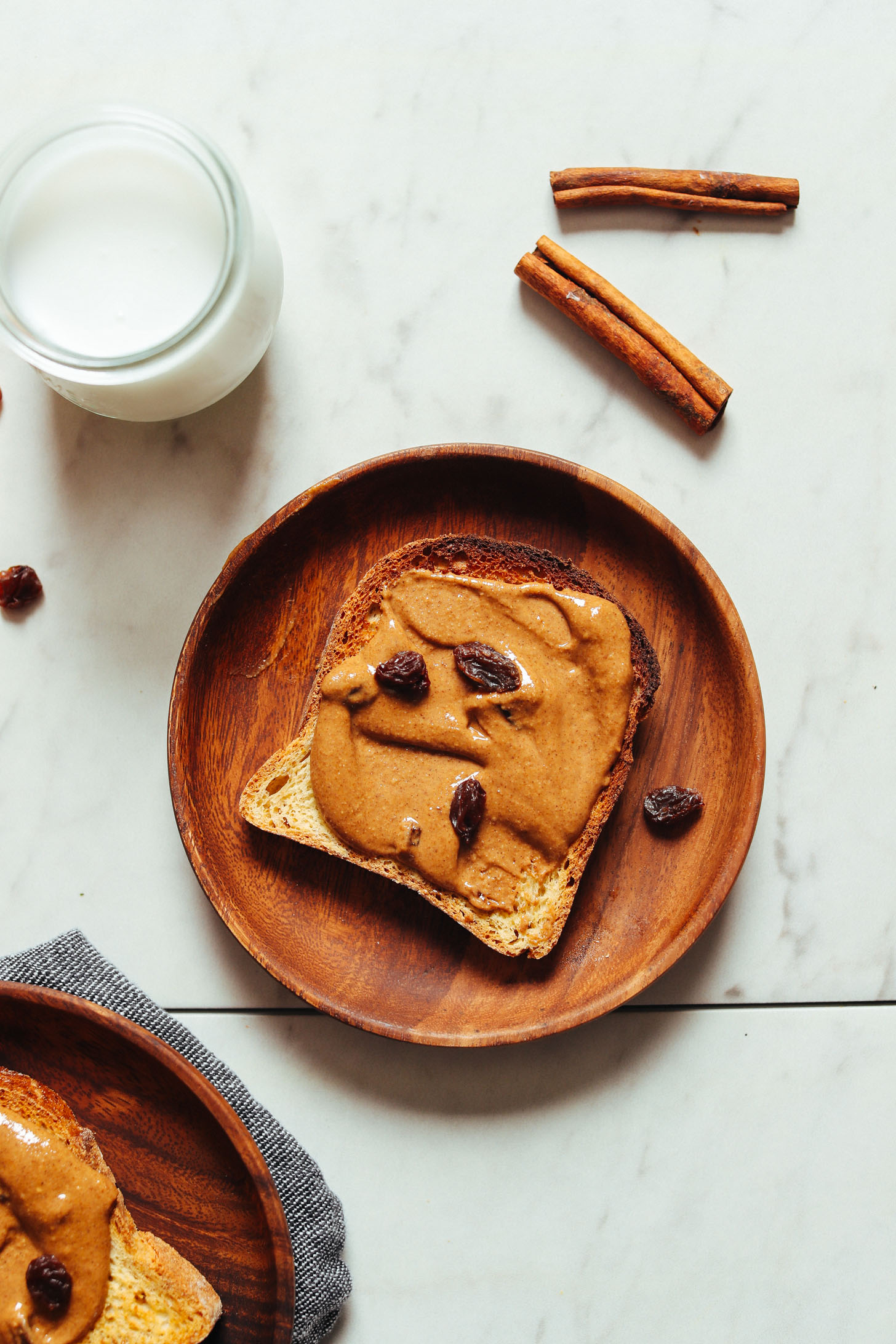 Plate of gluten-free toast with homemade Cinnamon Raisin Peanut Butter and a glass of dairy-free milk