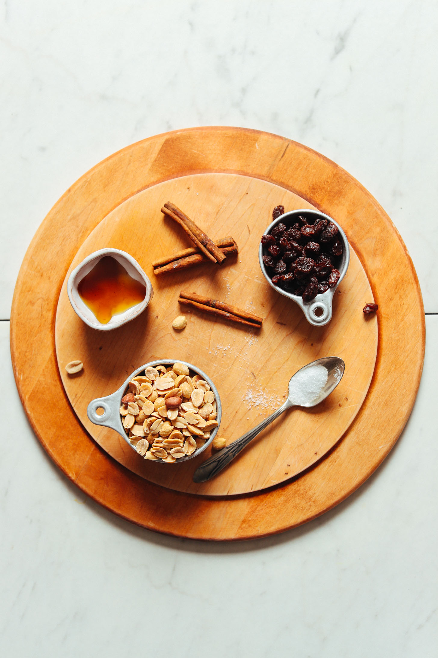 Wood cutting board with peanuts, maple syrup, stevia, raisins, and cinnamon for making our Cinnamon Raisin Peanut Butter recipe