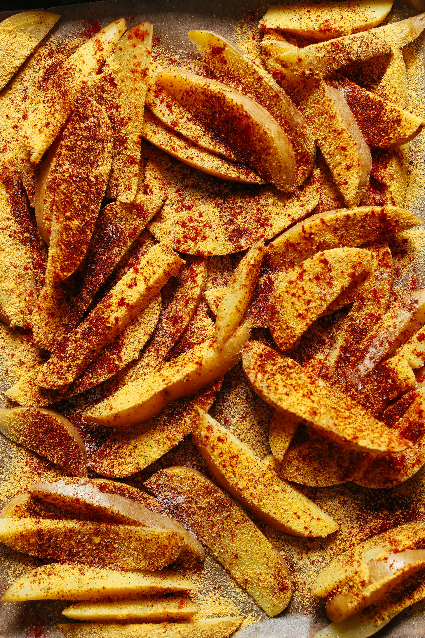 Parchment-lined baking sheet filled with potato wedges and seasonings for our Oil-Free Potato Fries recipe