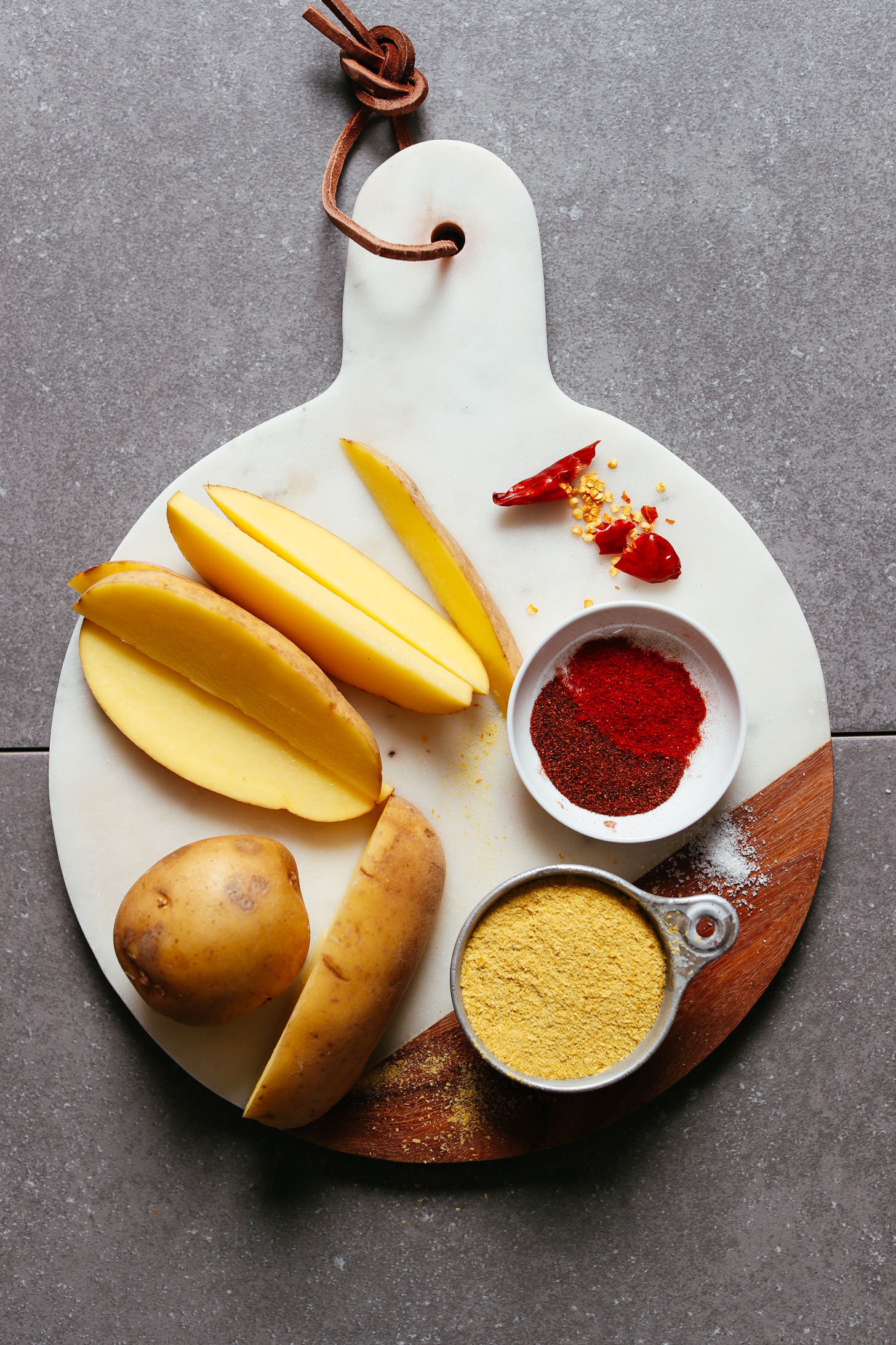 Marble cutting board featuring sliced potatoes, nutritional yeast, and spices for making healthy oil-free potato fries